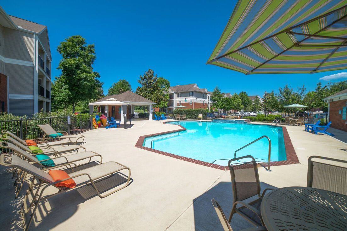 Swimming pool area with lounge chairs, umbrella, and small gazebo, on a sunny day.