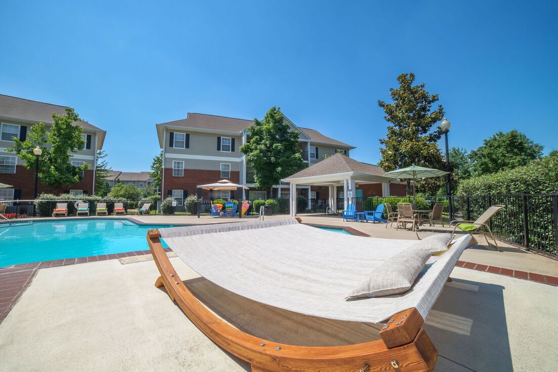 Swimming pool with a hammock and gazebo on a sunny day, with apartments in the background.