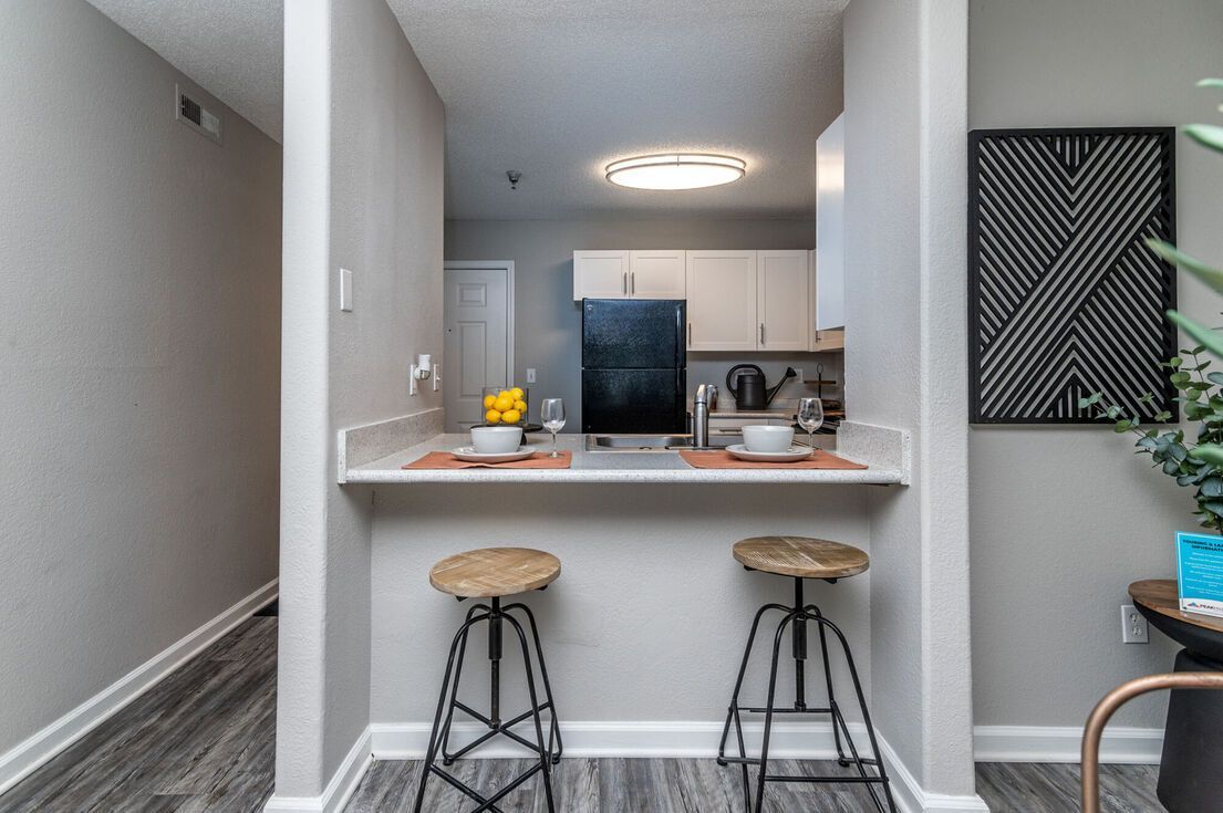 A small kitchen with a breakfast bar and two stools. Gray walls, a black refrigerator, and modern decor.