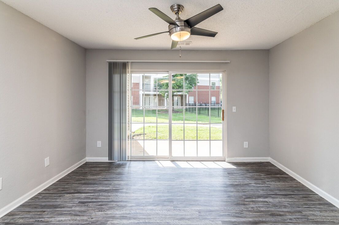 Empty room with gray walls, sliding glass door, ceiling fan, and wood-look flooring.