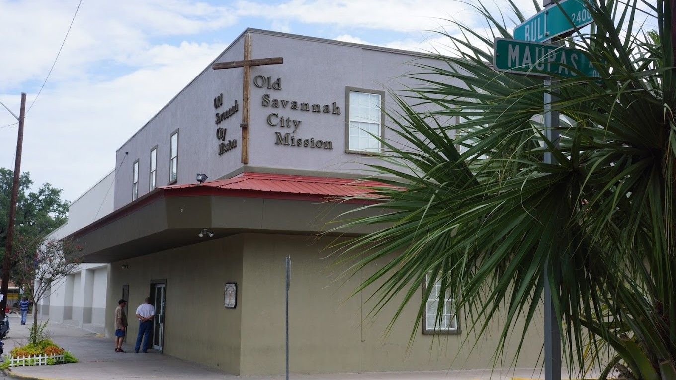 Old Savannah City Mission building on a street corner; beige facade, cross, palm tree, sign reads 