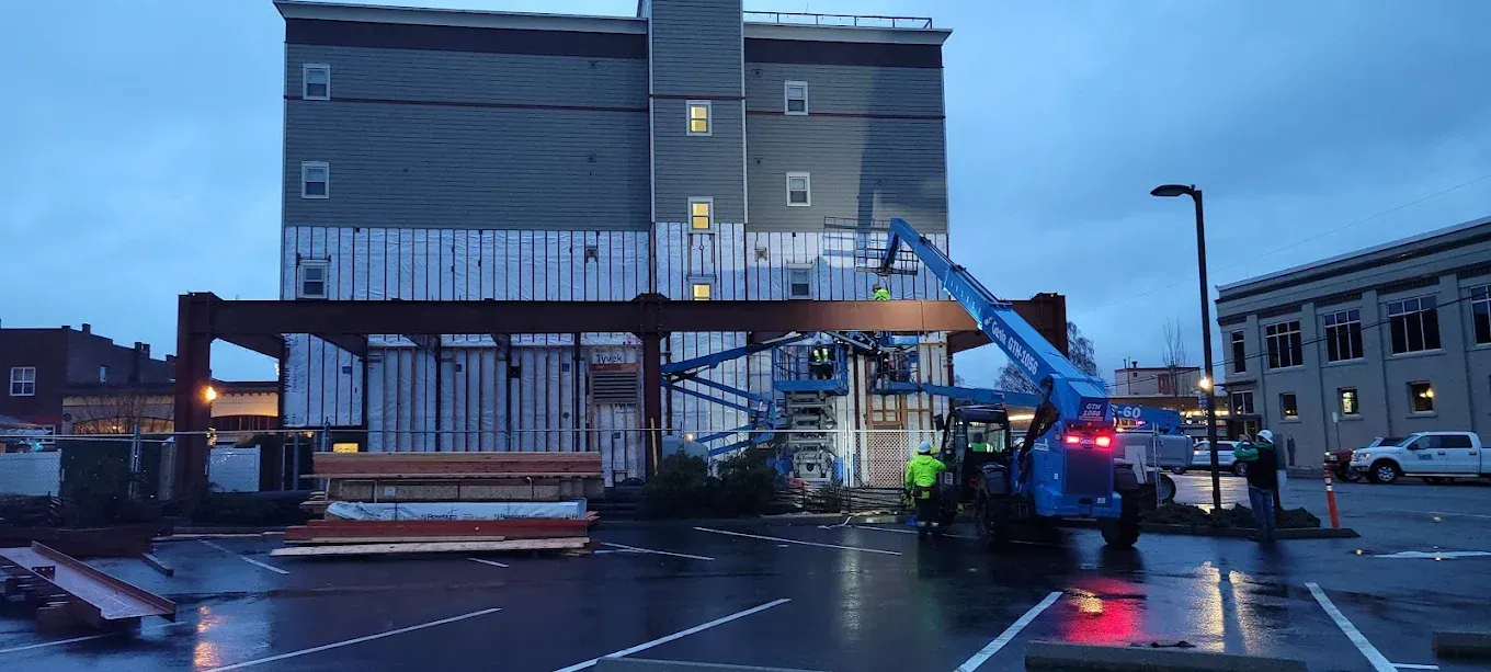 Construction work on a building exterior; a blue lift is extended towards it in a rainy parking lot.