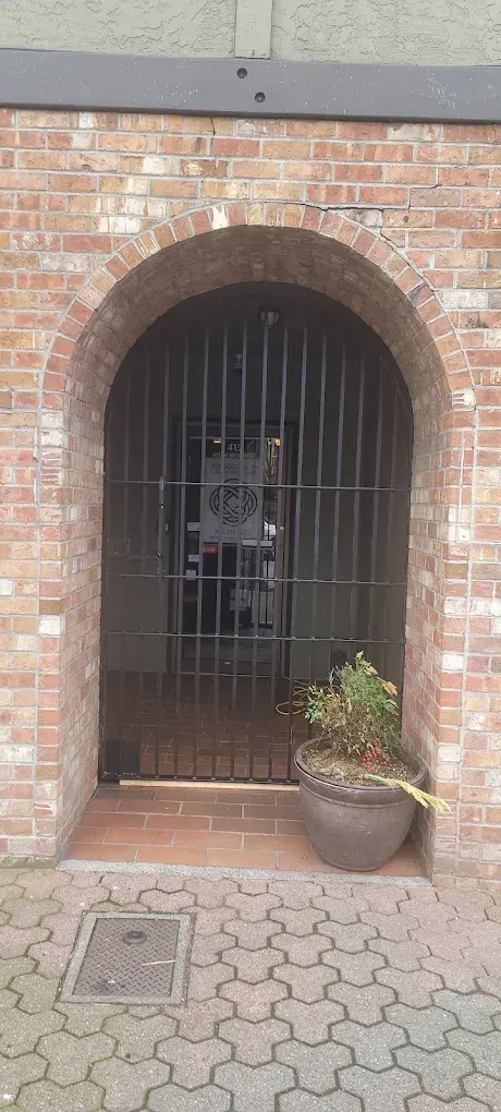 Brick arched doorway with metal gate; potted plant to the right; brick building with patterned pavement.
