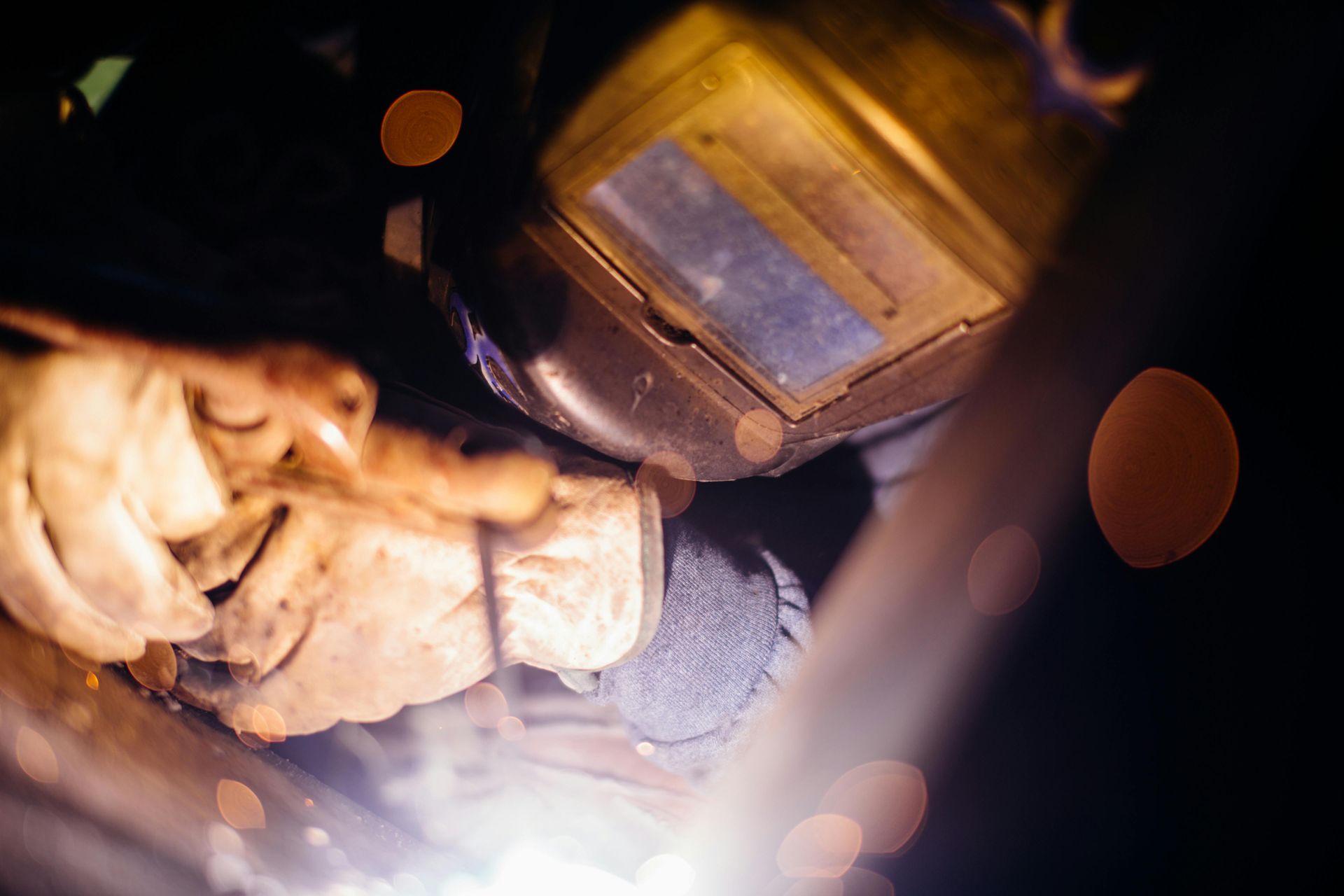 Welder wearing helmet and gloves, working with a bright light in a dark setting.