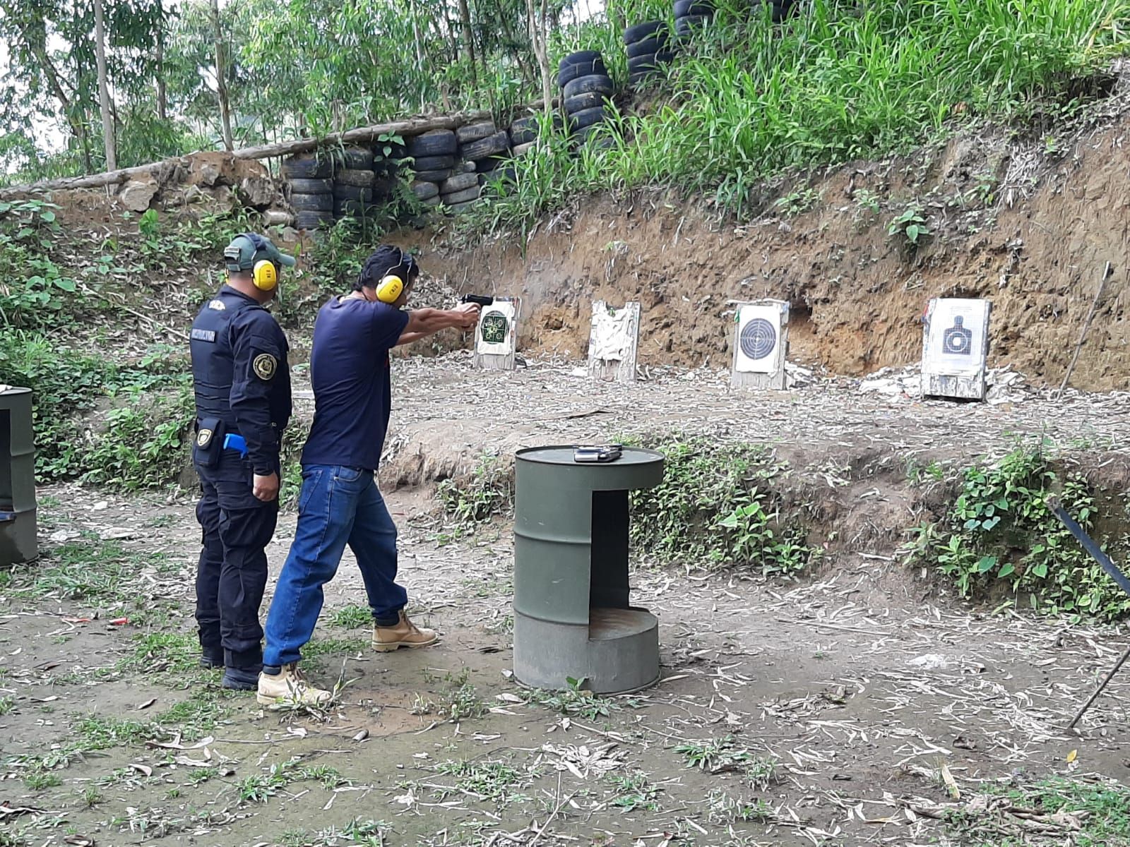 Hombre disparando una pistola a objetivos con un instructor en un campo de tiro al aire libre.