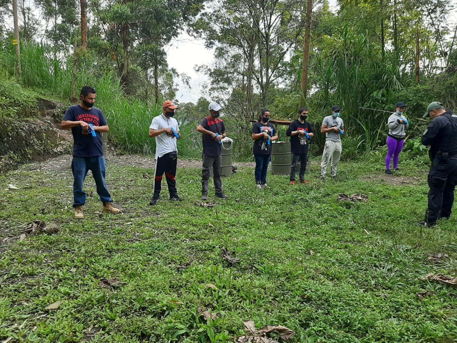 Un grupo de personas en una zona verde, algunas con objetos en la mano. Bosque al fondo.