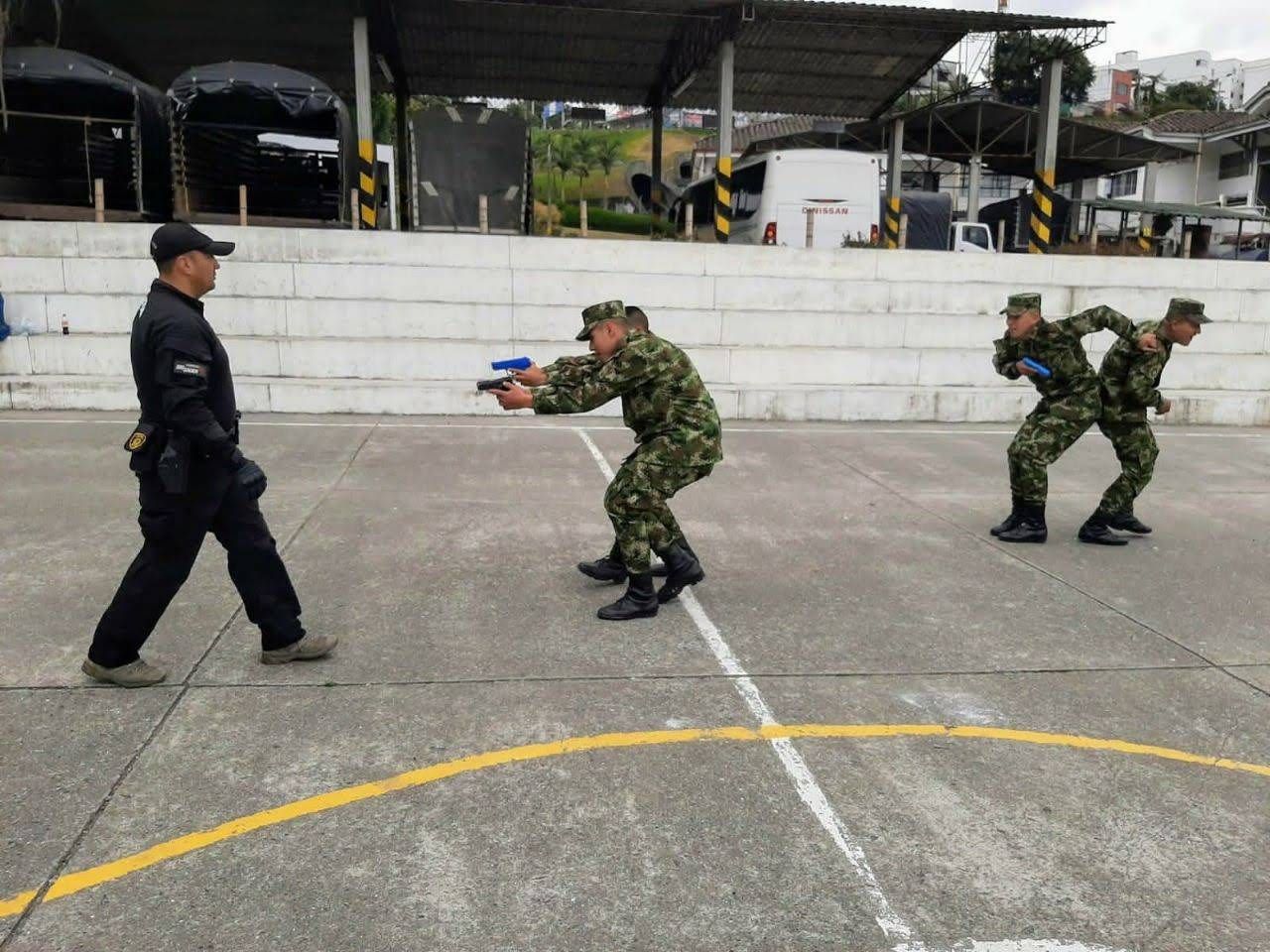 Soldados en entrenamiento de camuflaje con armas de fuego al aire libre, bajo la supervisión de un oficial de policía.