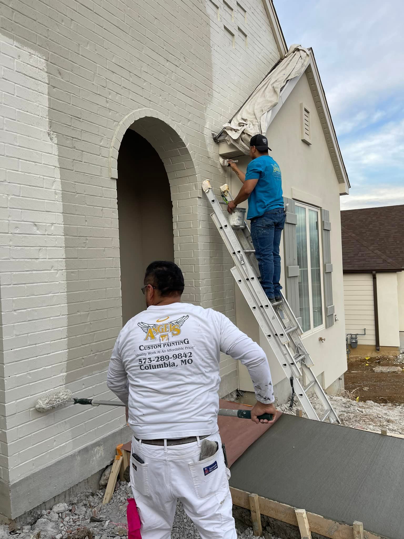 Two men are painting a white brick house.
