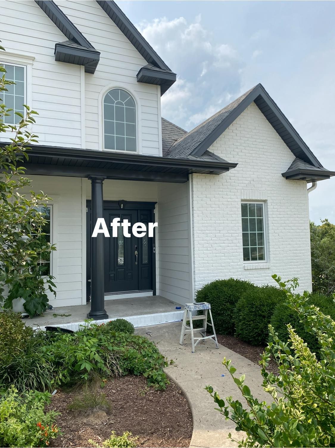 A white brick house with black trim and a black door has been painted white.