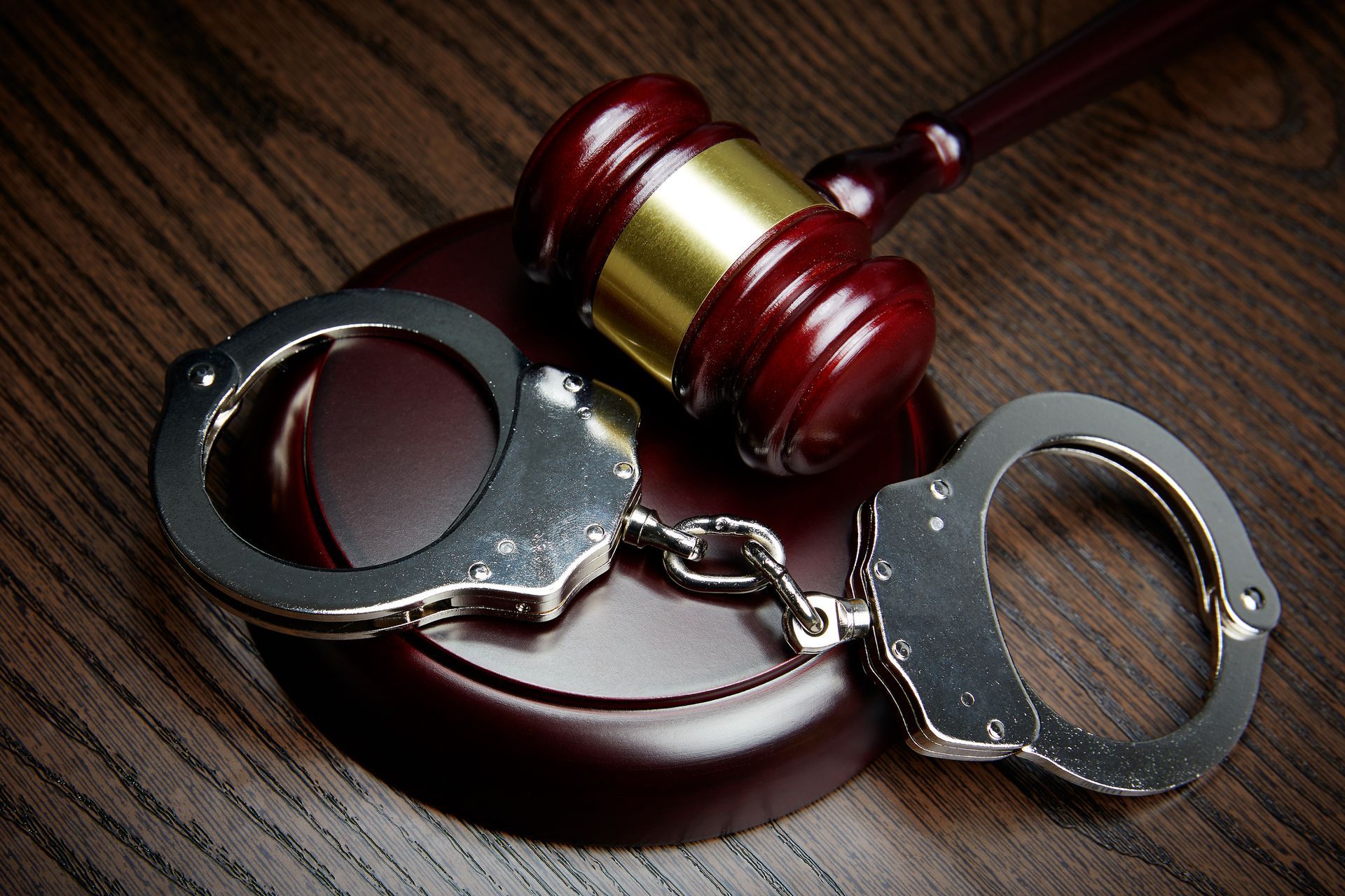 A pair of handcuffs and a judge 's gavel on a wooden table.