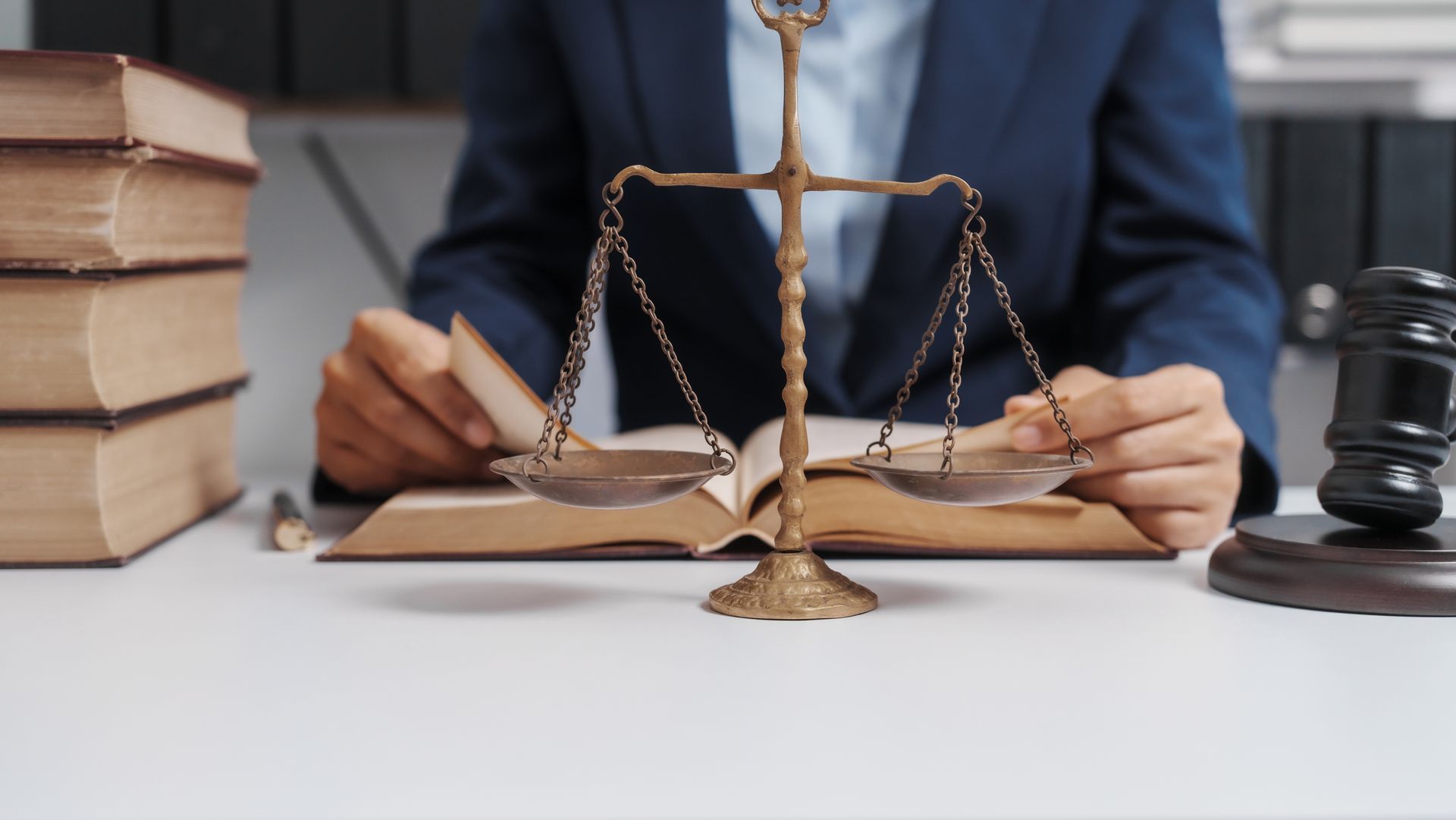Scales of justice on a desk with open law books and a gavel in the background. Scales of justice on a desk with open law books and a gavel in the background.