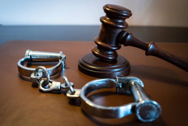 A pair of handcuffs and a judge 's gavel on a wooden table.