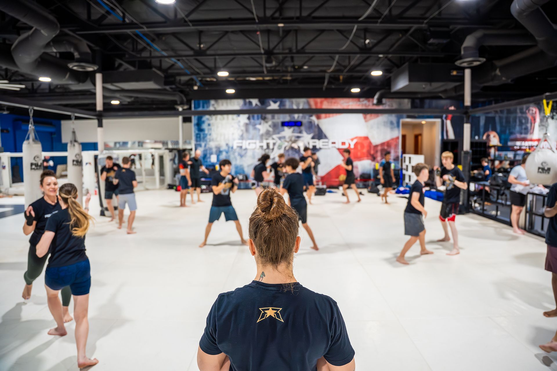 People practicing martial arts in a large gym with white mats and blue walls