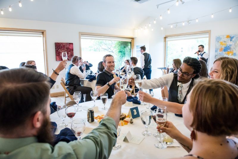People toasting with champagne at a wedding reception. Bright room with tables set for dinner.