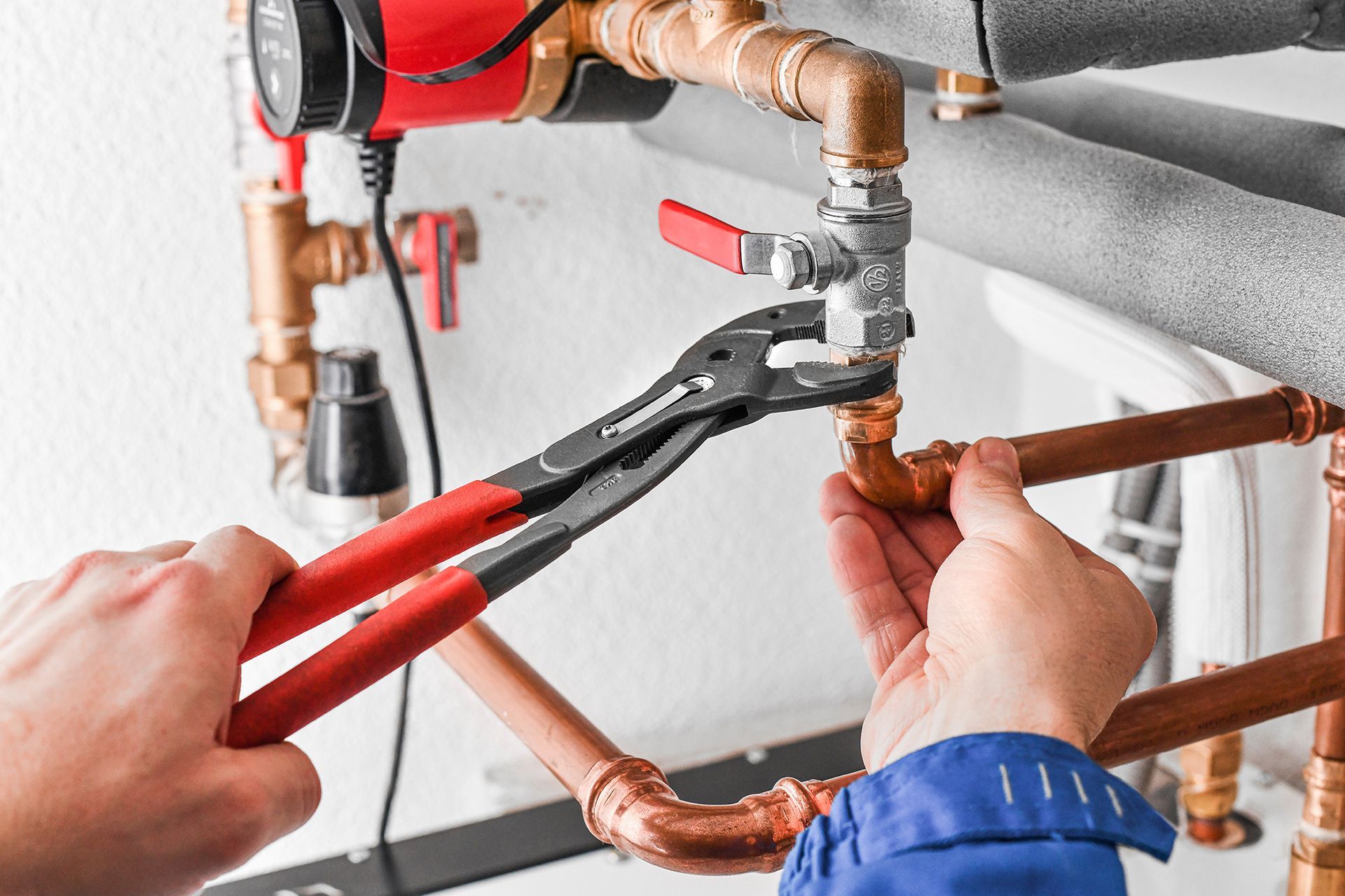 A plumber is fixing a pipe with a pair of pliers.