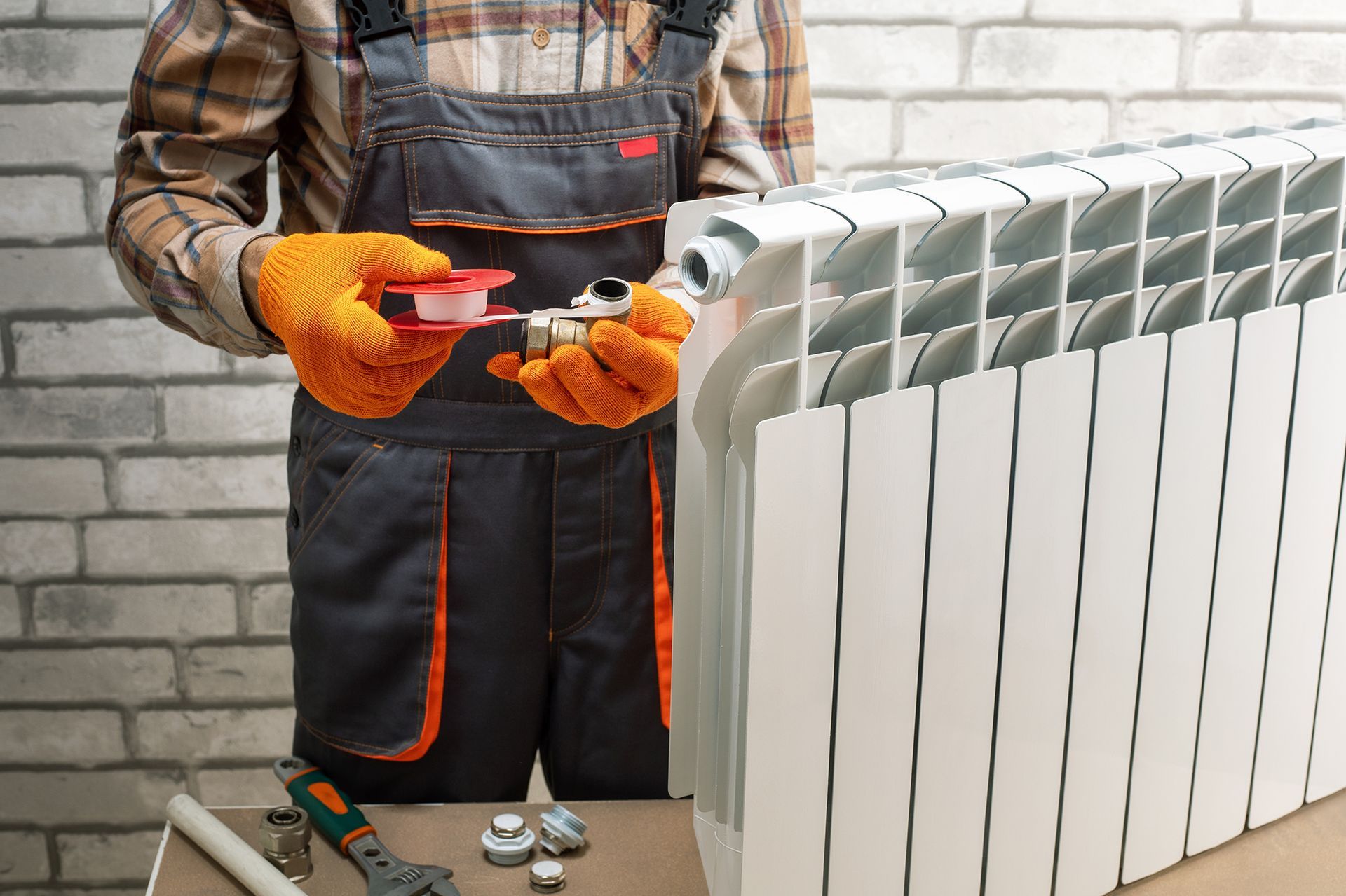 A man is fixing a radiator with a wrench.