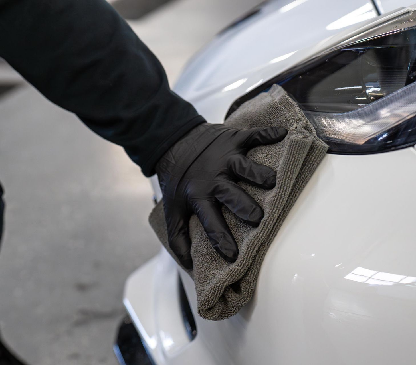 A person wearing black gloves is cleaning a white car with a cloth