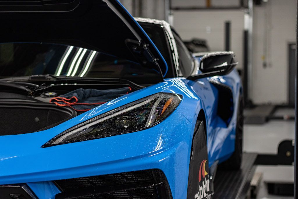 A blue sports car with the hood up is parked in a garage.