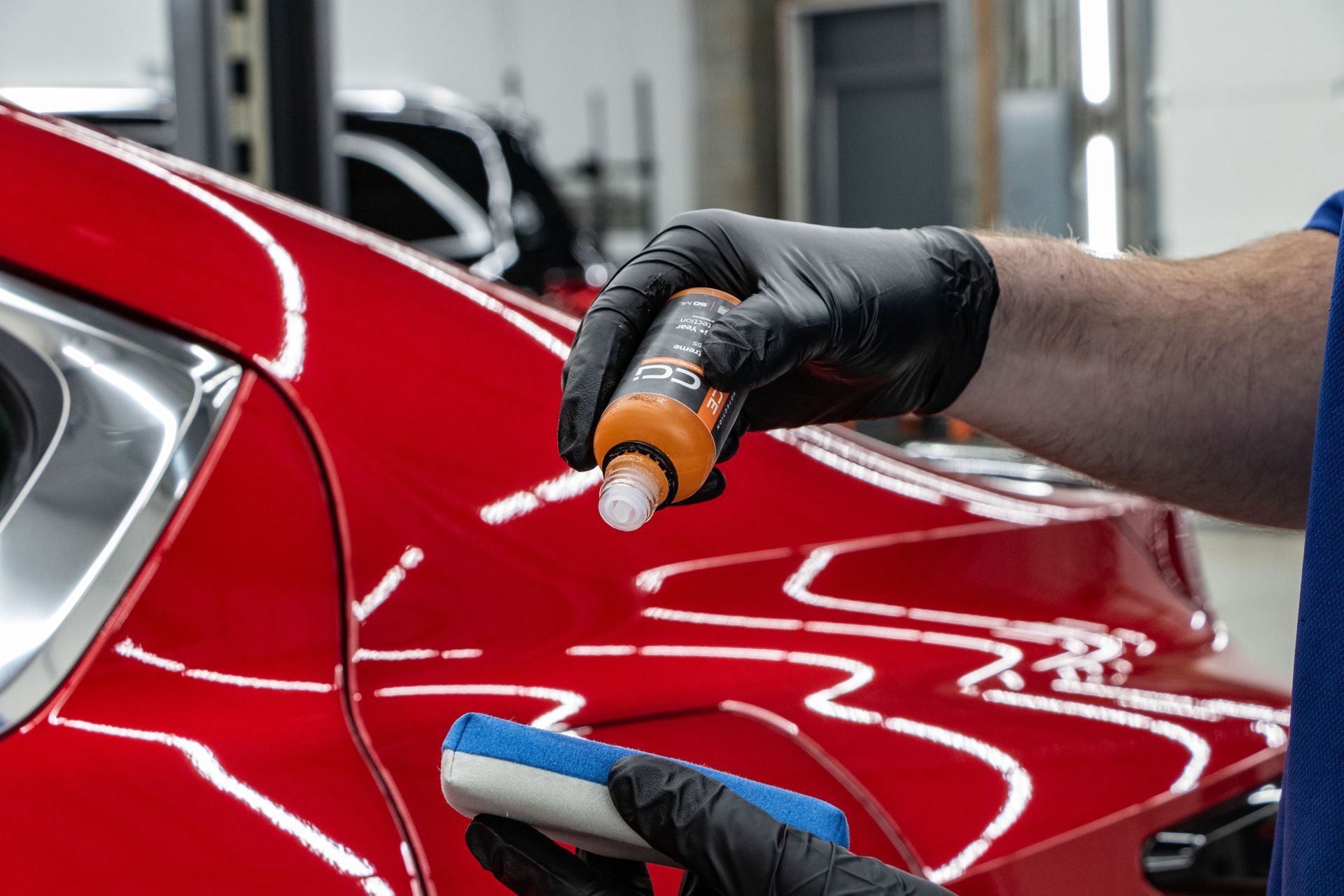 A person is applying a coating to a red car.