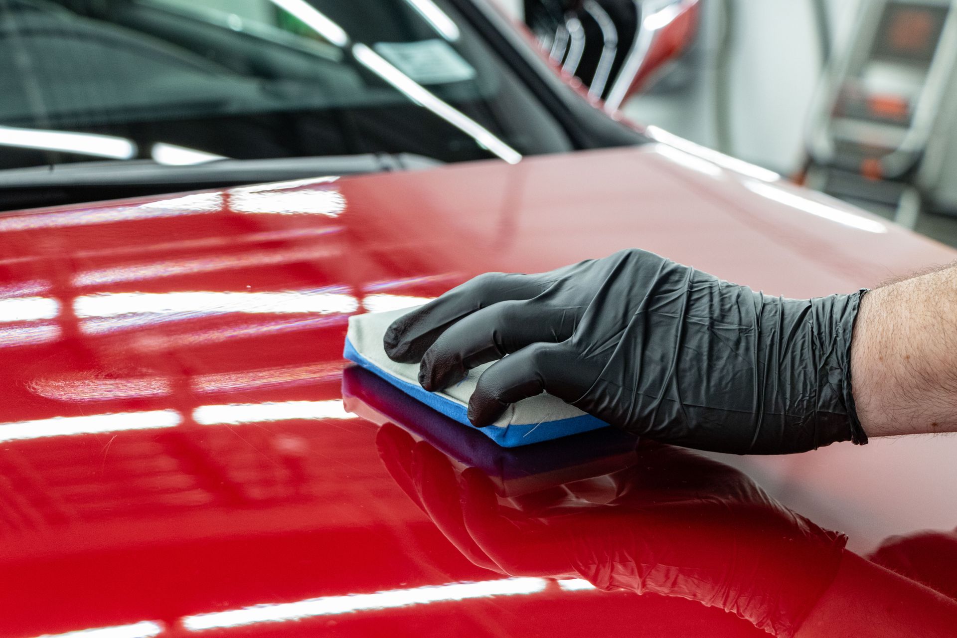 A person wearing black gloves is cleaning a car with a brush.