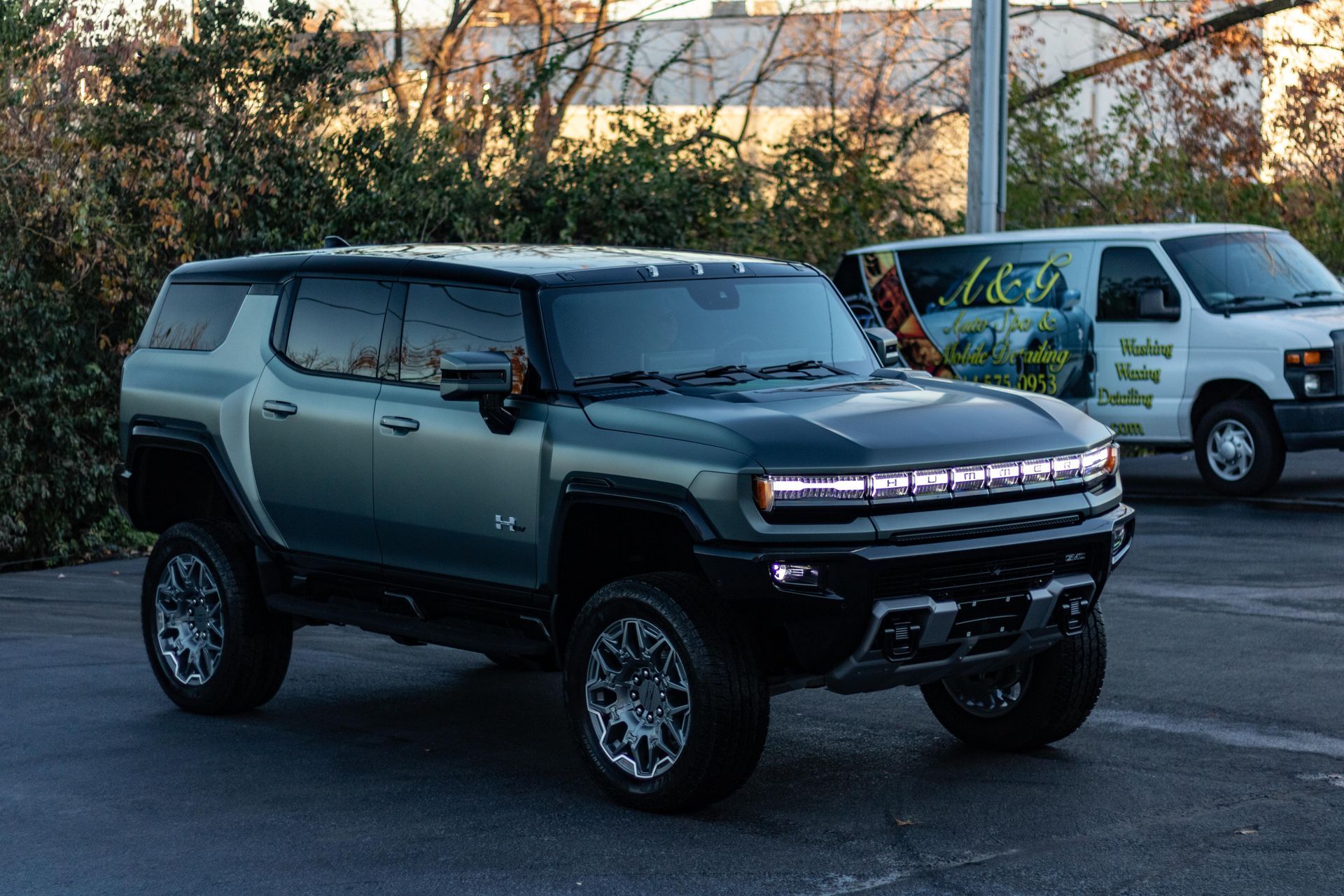 A hummer suv is parked in a parking lot next to a white van.