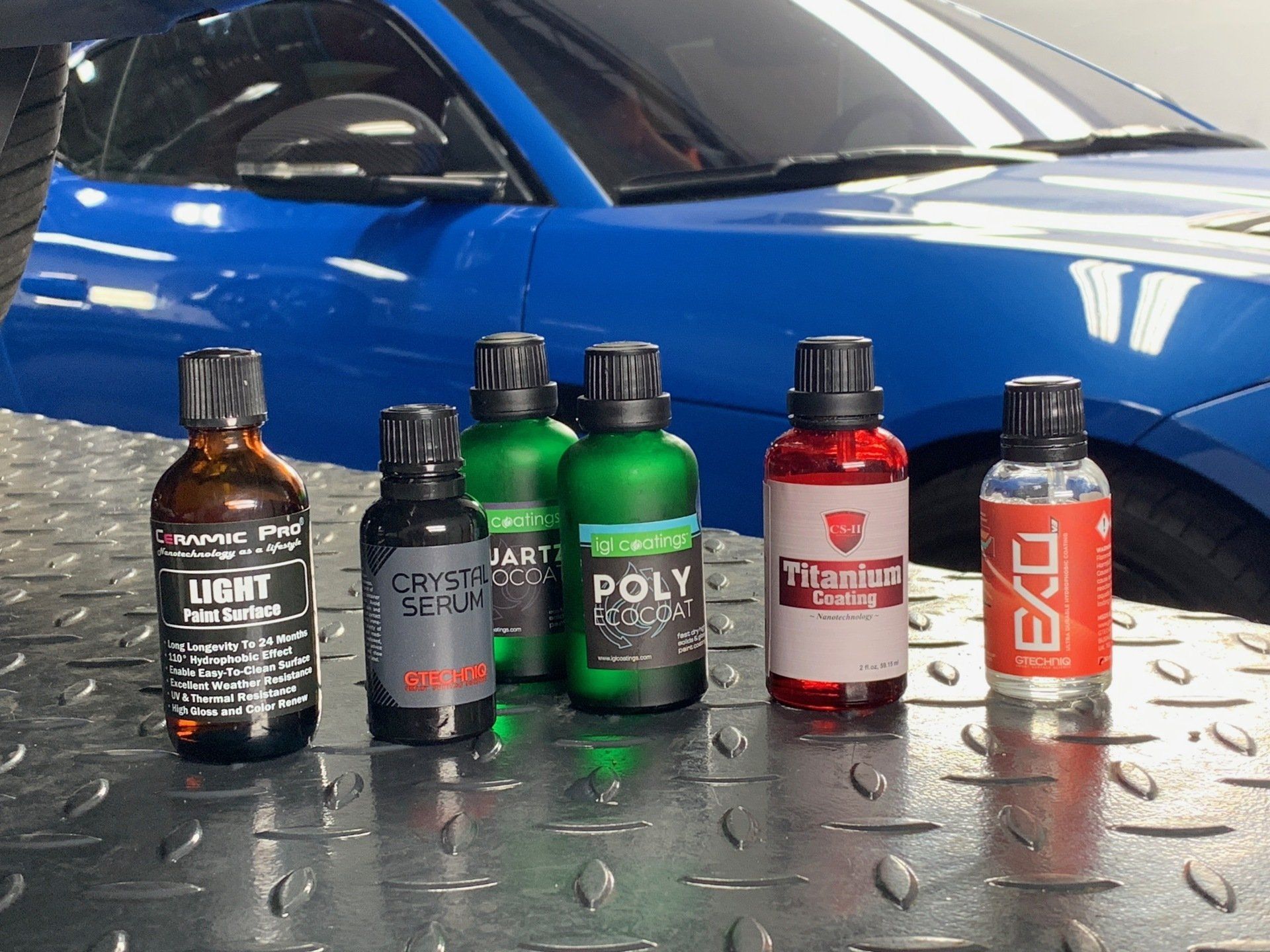 Several bottles of chemicals are sitting in front of a blue car