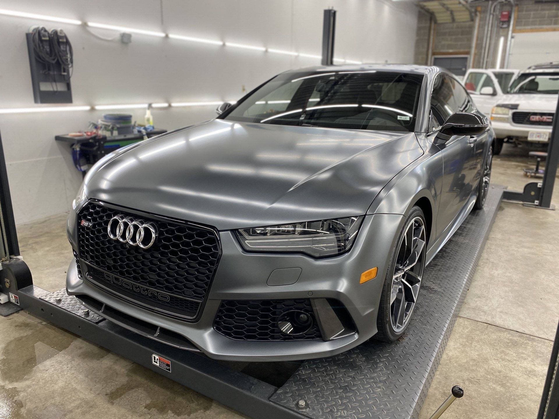 A gray audi rs7 is parked on a lift in a garage.