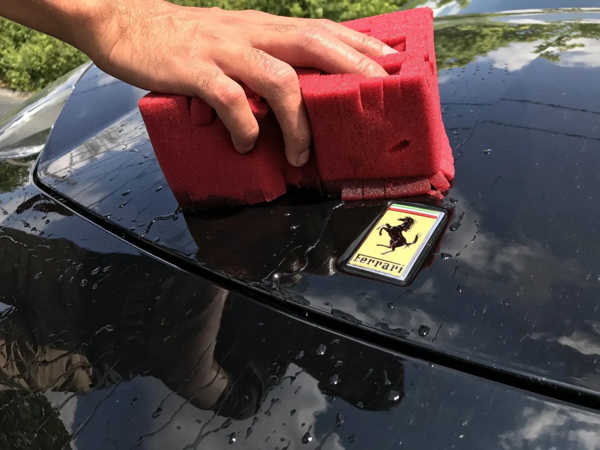 A person is cleaning a Ferrari car with a red sponge