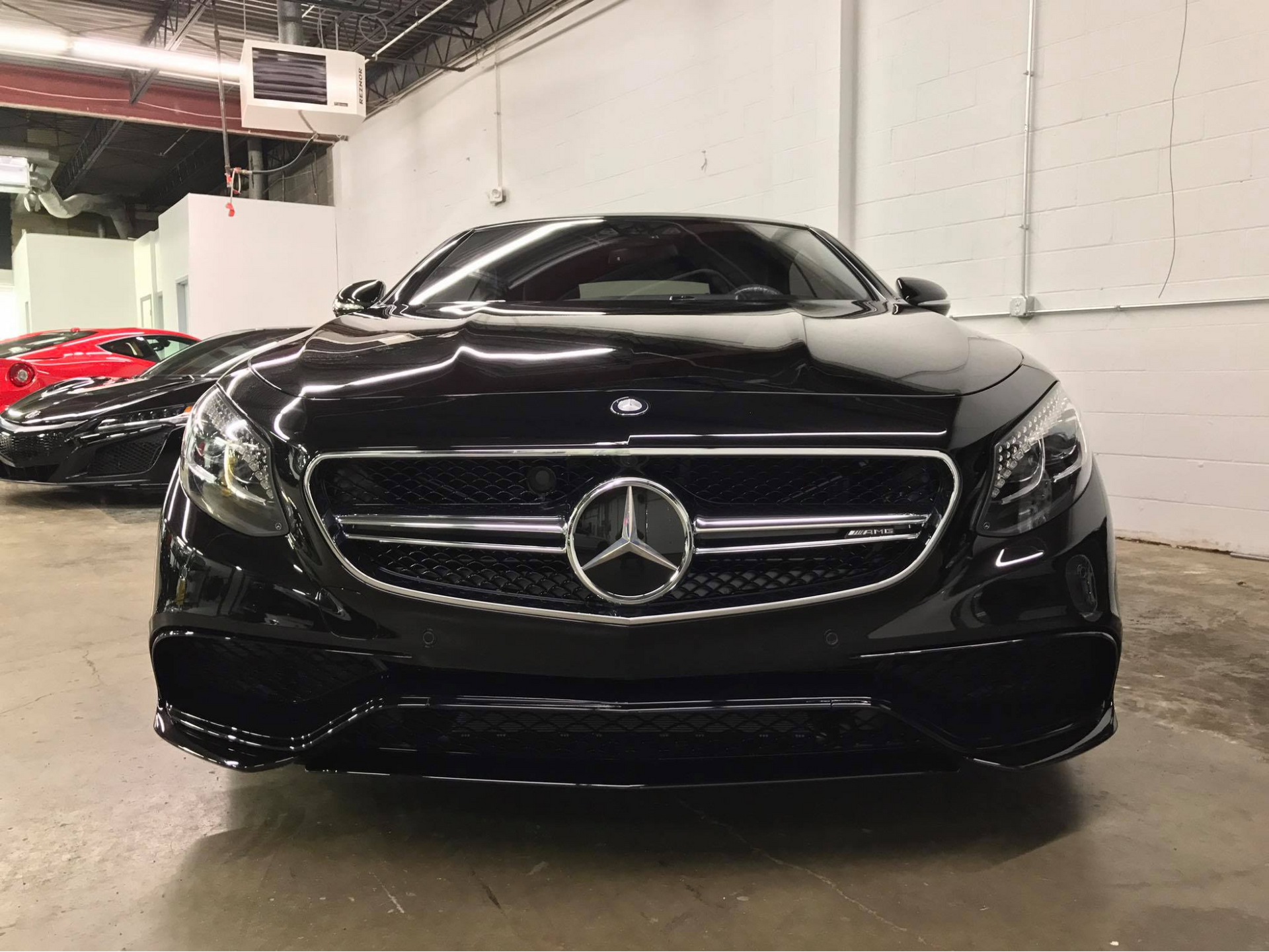 Black Mercedes-Benz coupe in a showroom, front view, shiny paint. Another car is partially visible in the background.