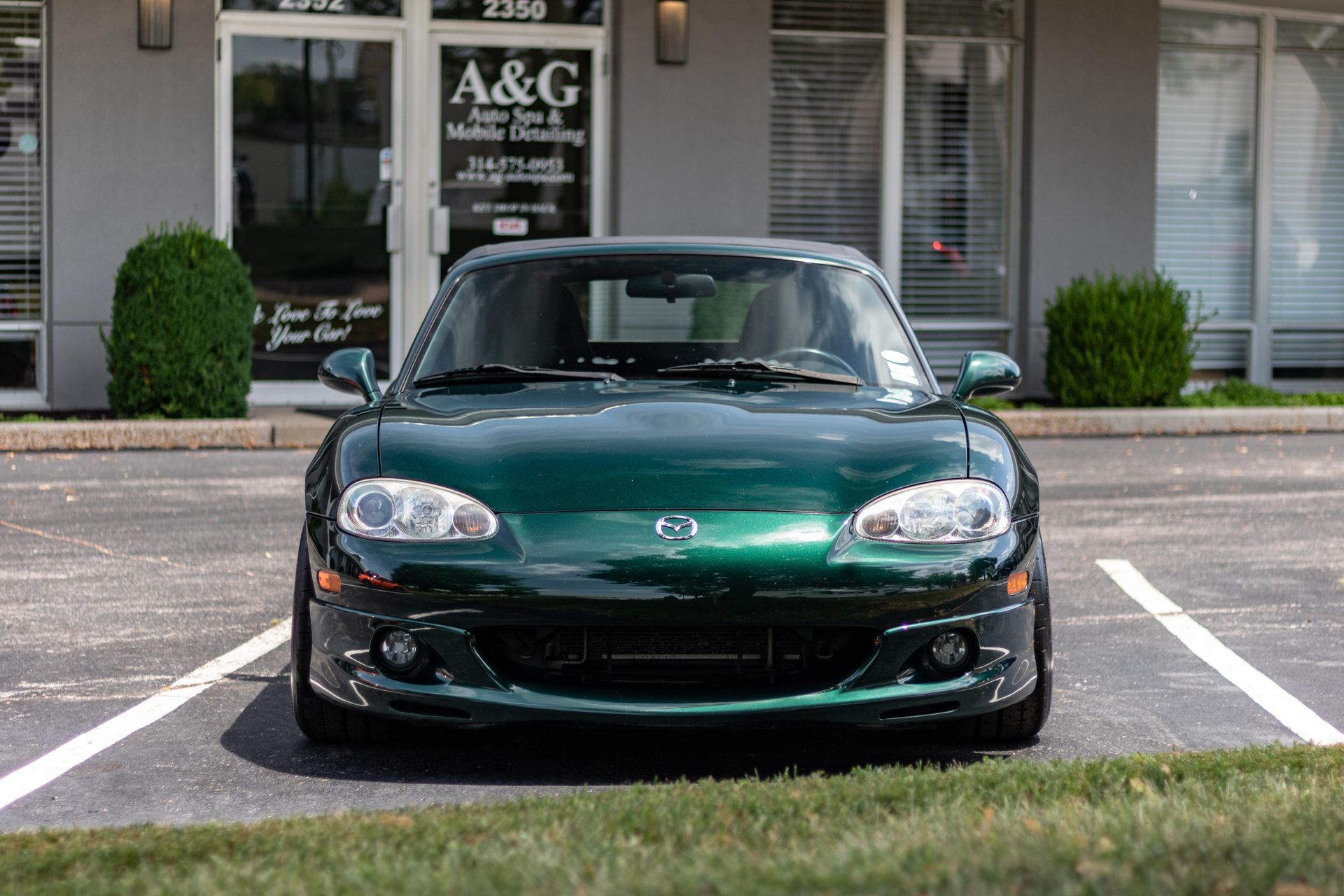 A green sports car is parked in a parking lot in front of a building.