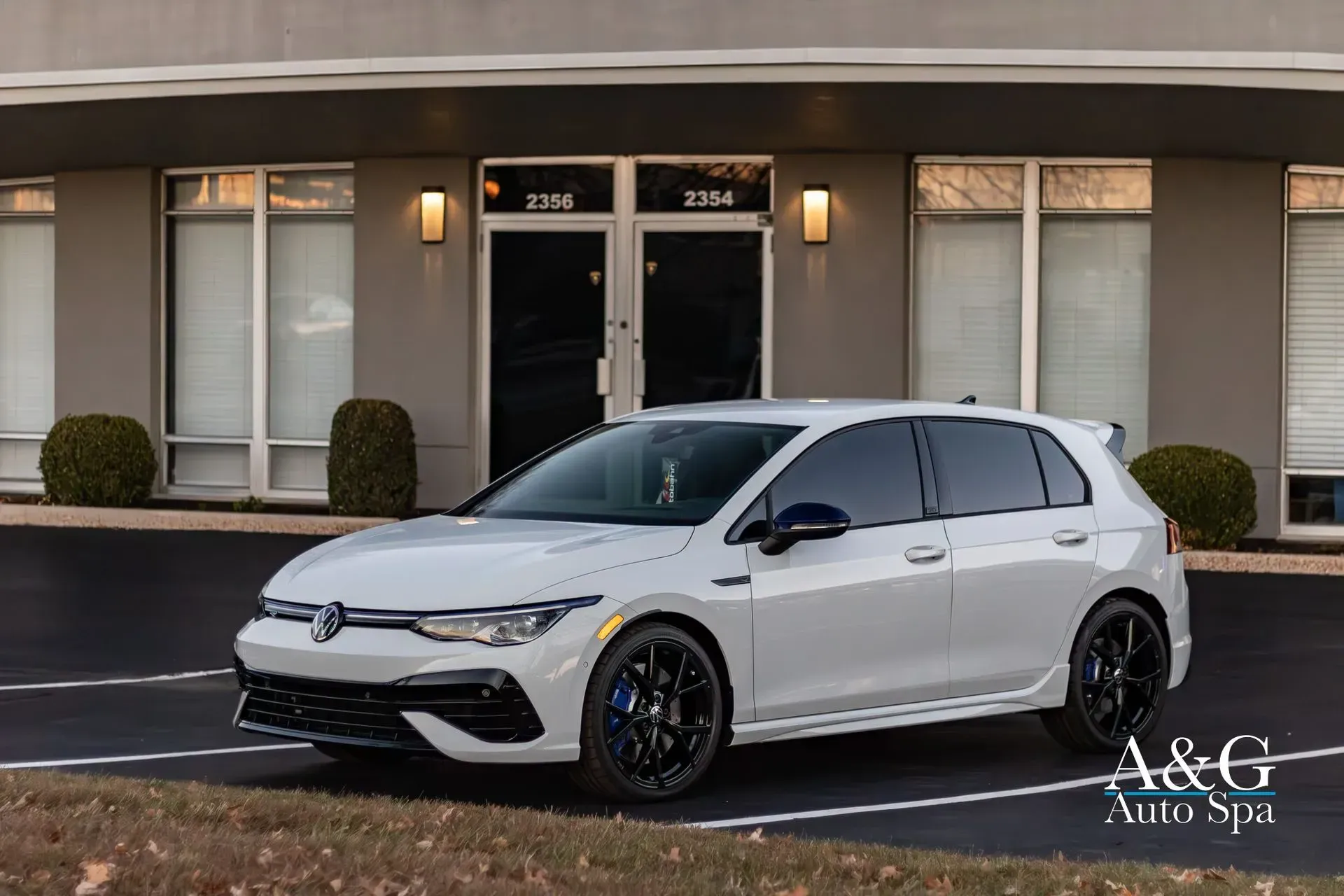 A white volkswagen golf r is parked in front of a building.