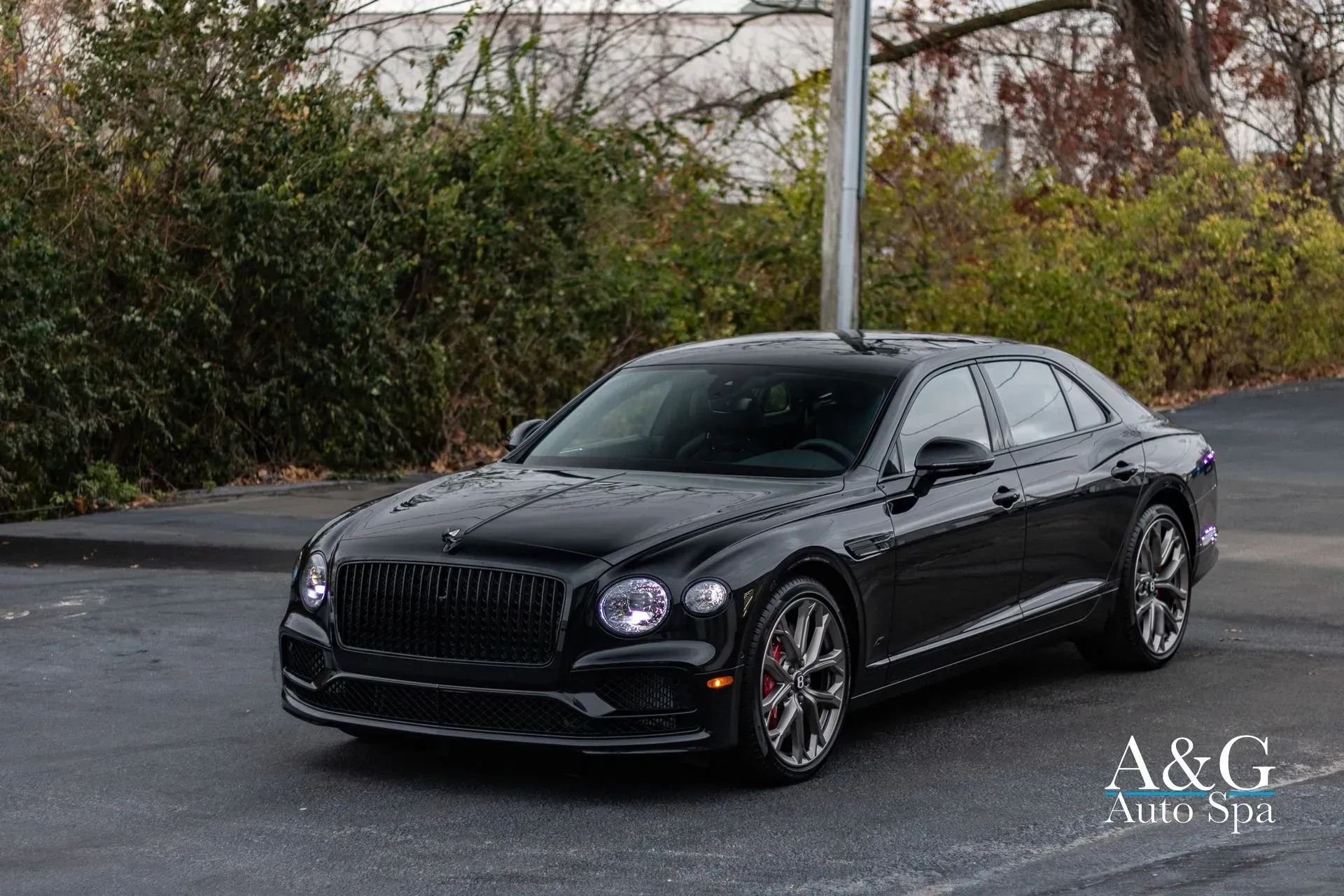 A black bentley flying spur is parked in a parking lot.