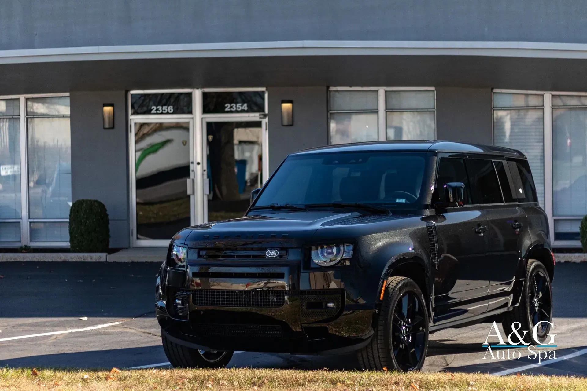 A black land rover defender is parked in front of a building.