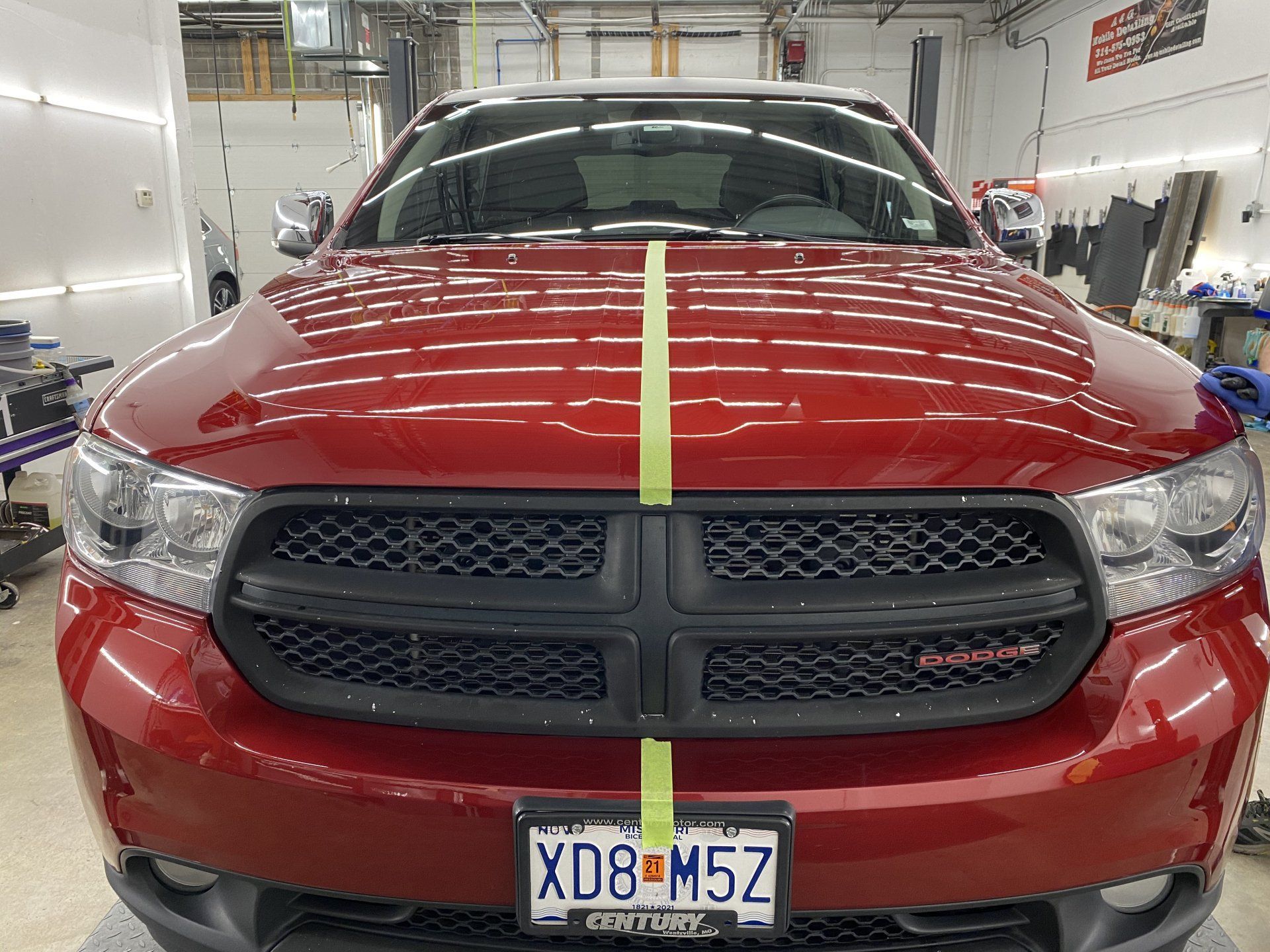 A red dodge ram is sitting in a garage with a yellow tape on the hood.