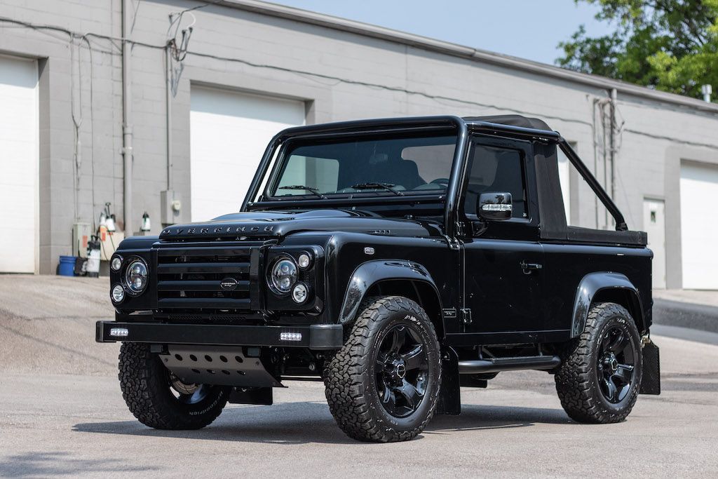 A black land rover defender is parked in front of a building.