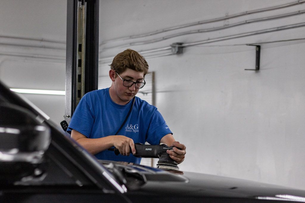 A man is polishing the hood of a car in a garage.