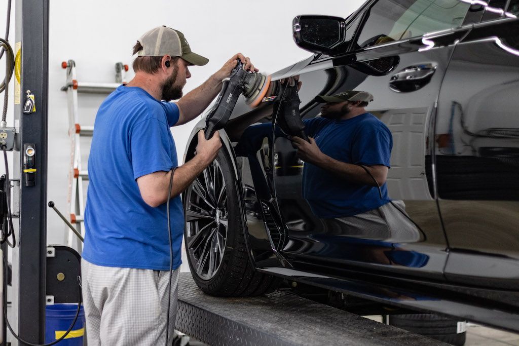 A man is polishing a black car in a garage.