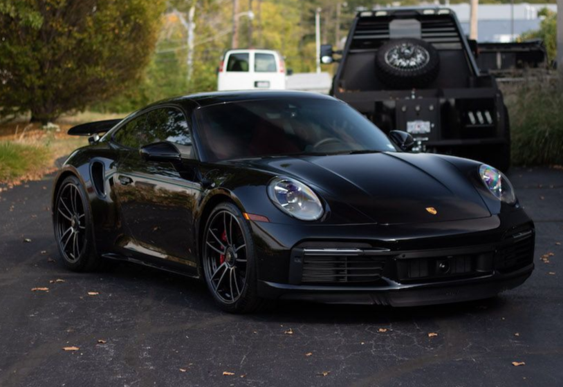 A black porsche 911 is parked in a driveway next to a truck.