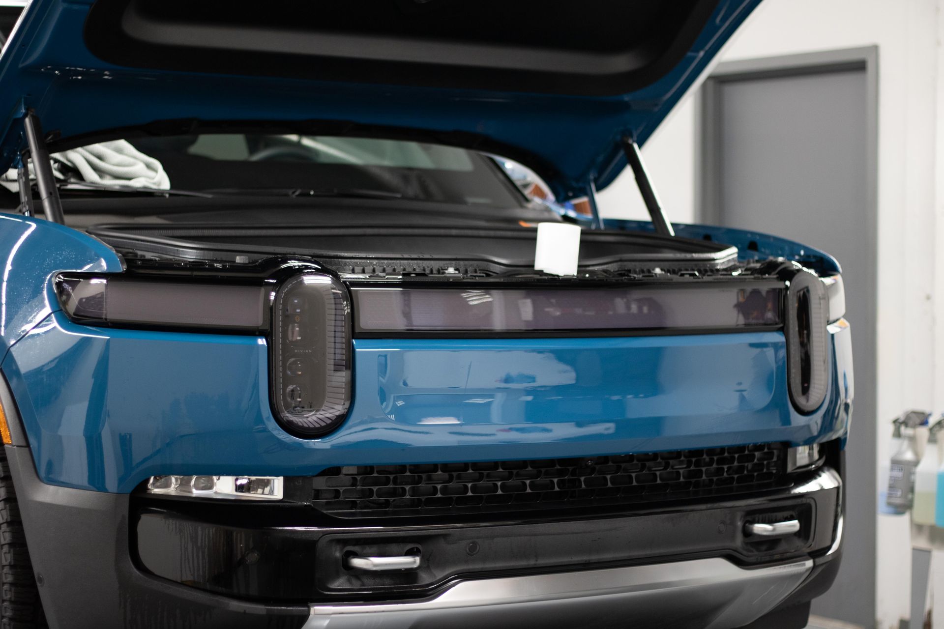 A blue truck with the hood open is sitting in a garage.