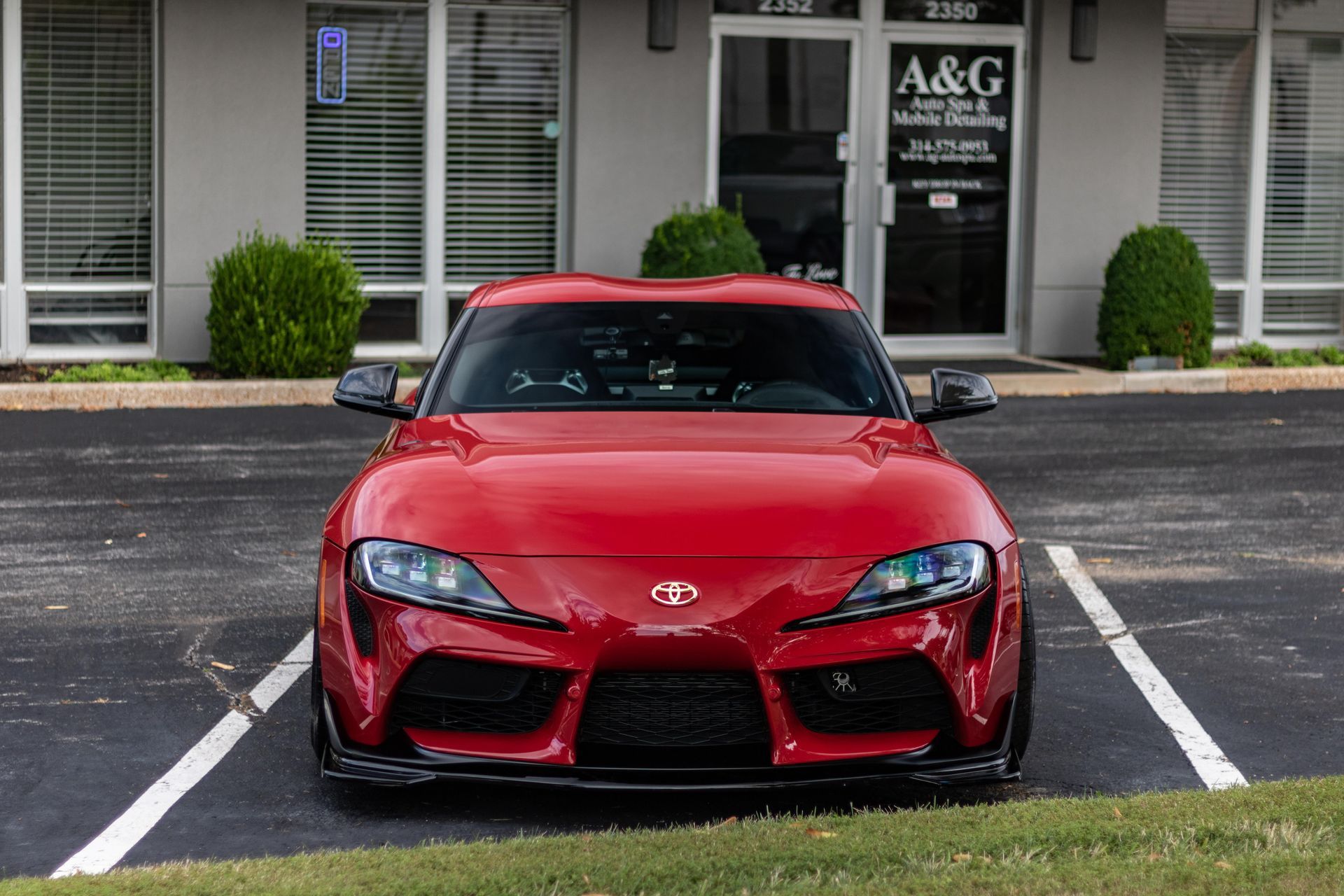 A red toyota supra is parked in a parking lot in front of a building.