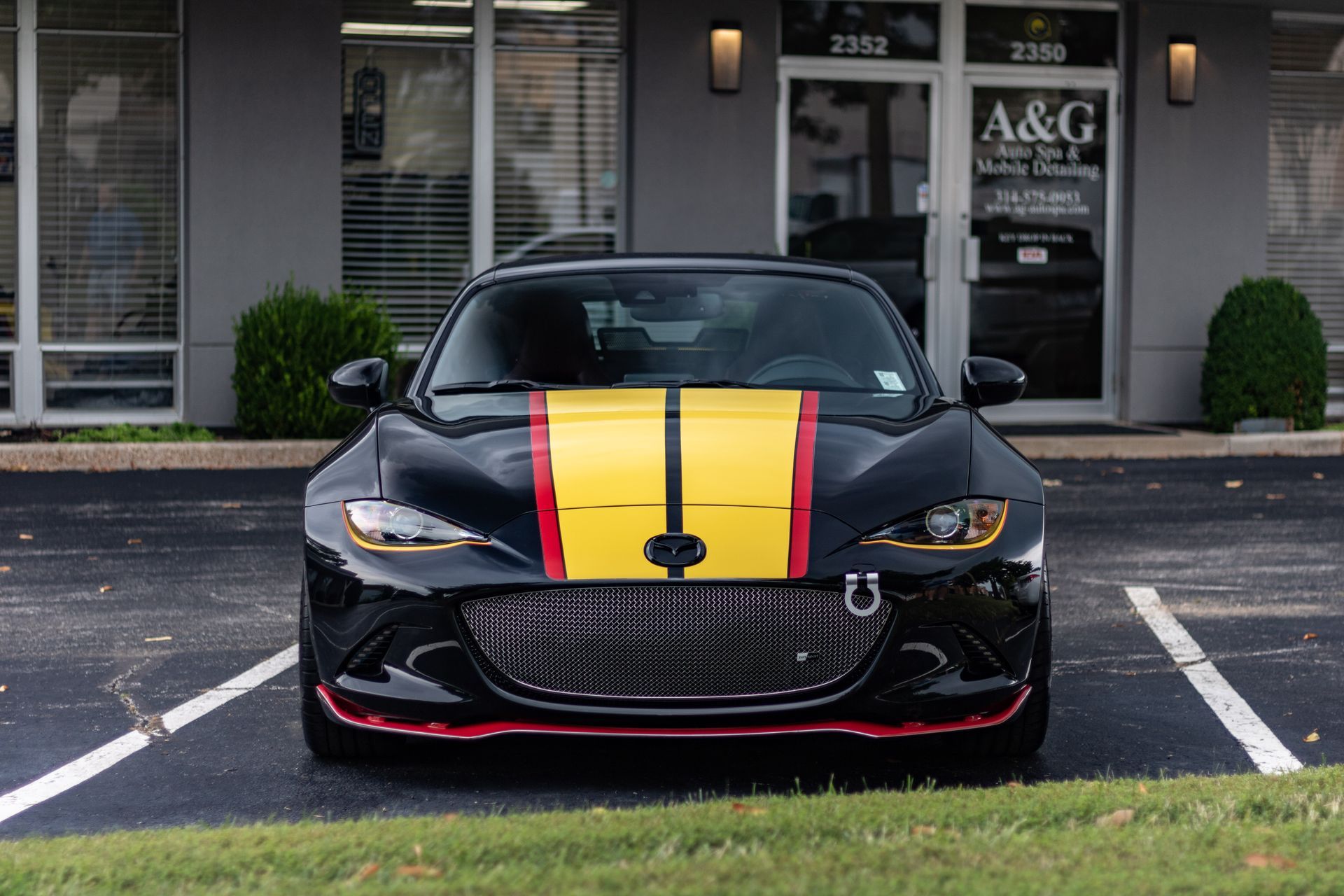 A black sports car with yellow and red stripes is parked in a parking lot in front of a building.