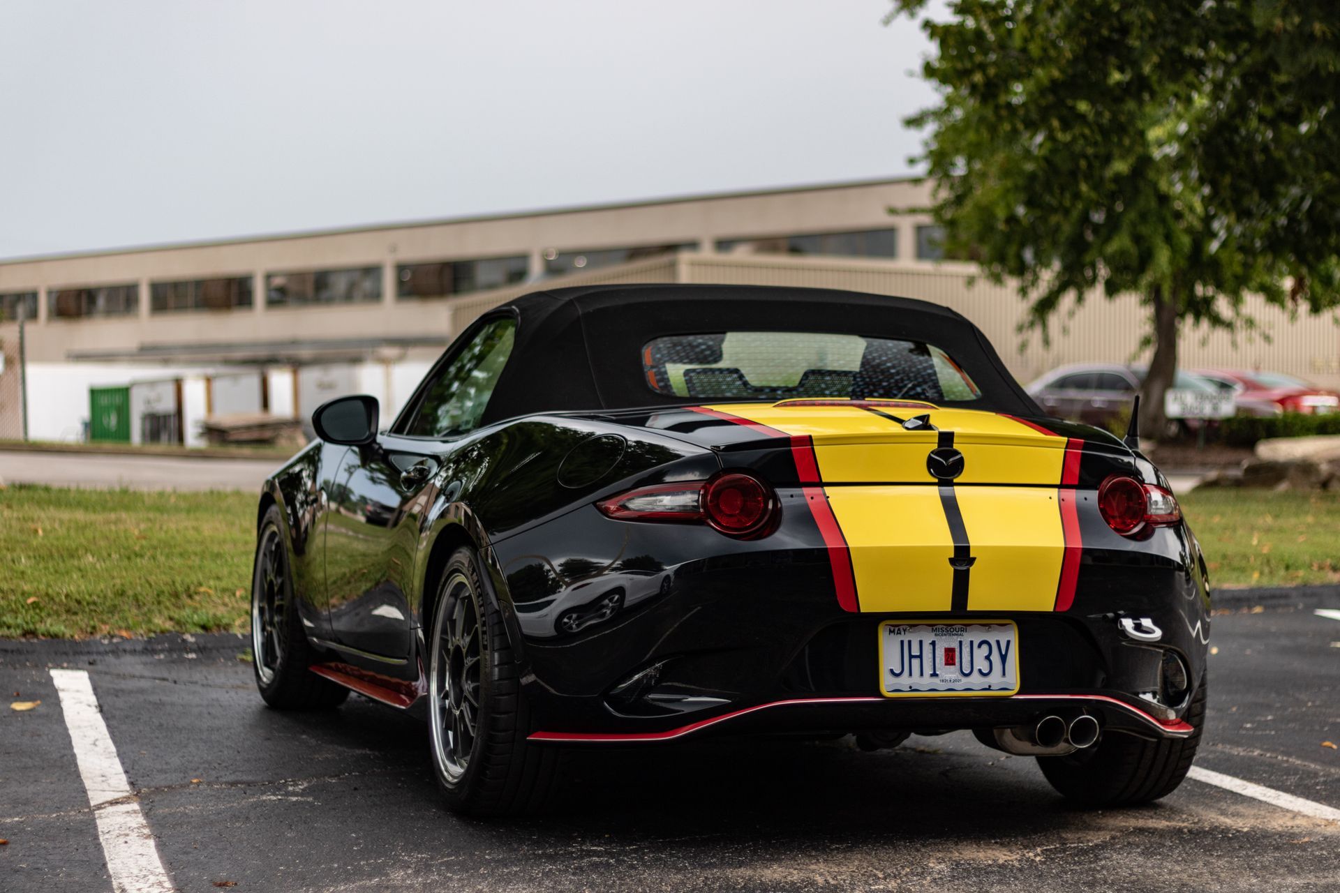 Black convertible car with a yellow and black racing stripe, parked in a parking lot.
