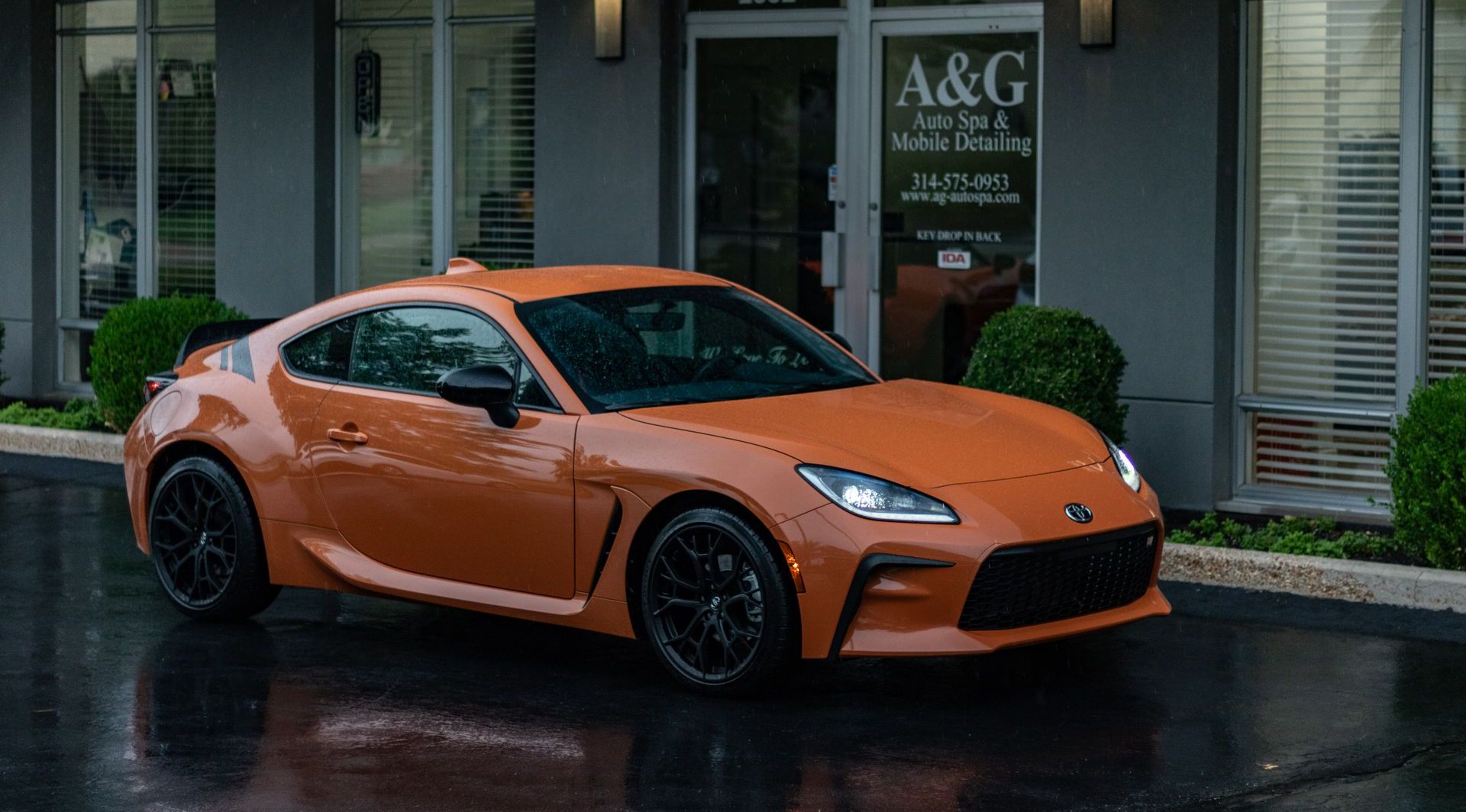 A toyota scion fr s is parked in front of a building in the rain.
