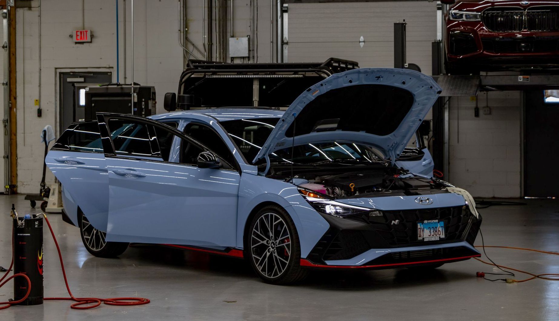 A blue car is parked in a garage with its hood open.