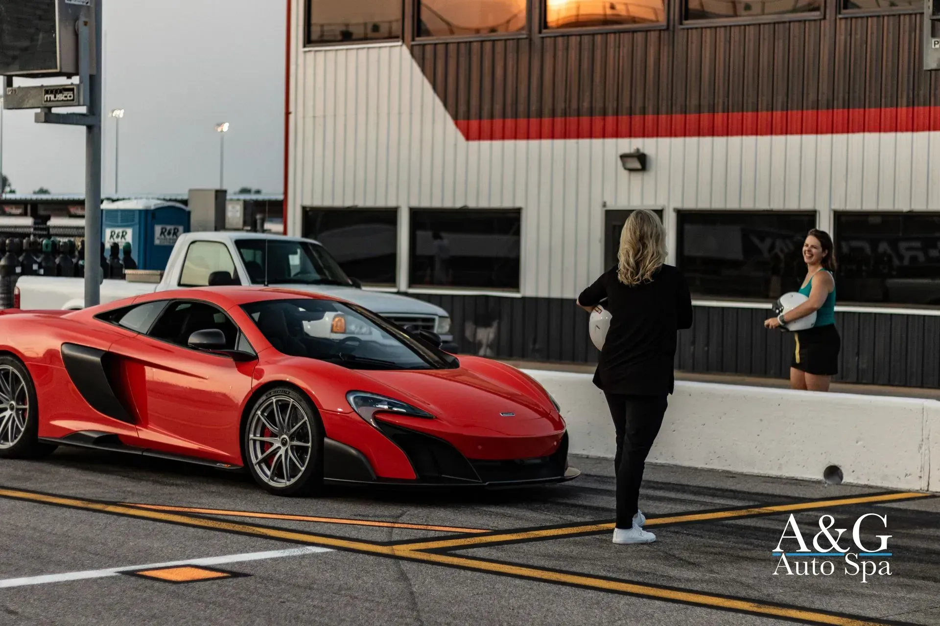 A woman is standing next to a red sports car in a parking lot.