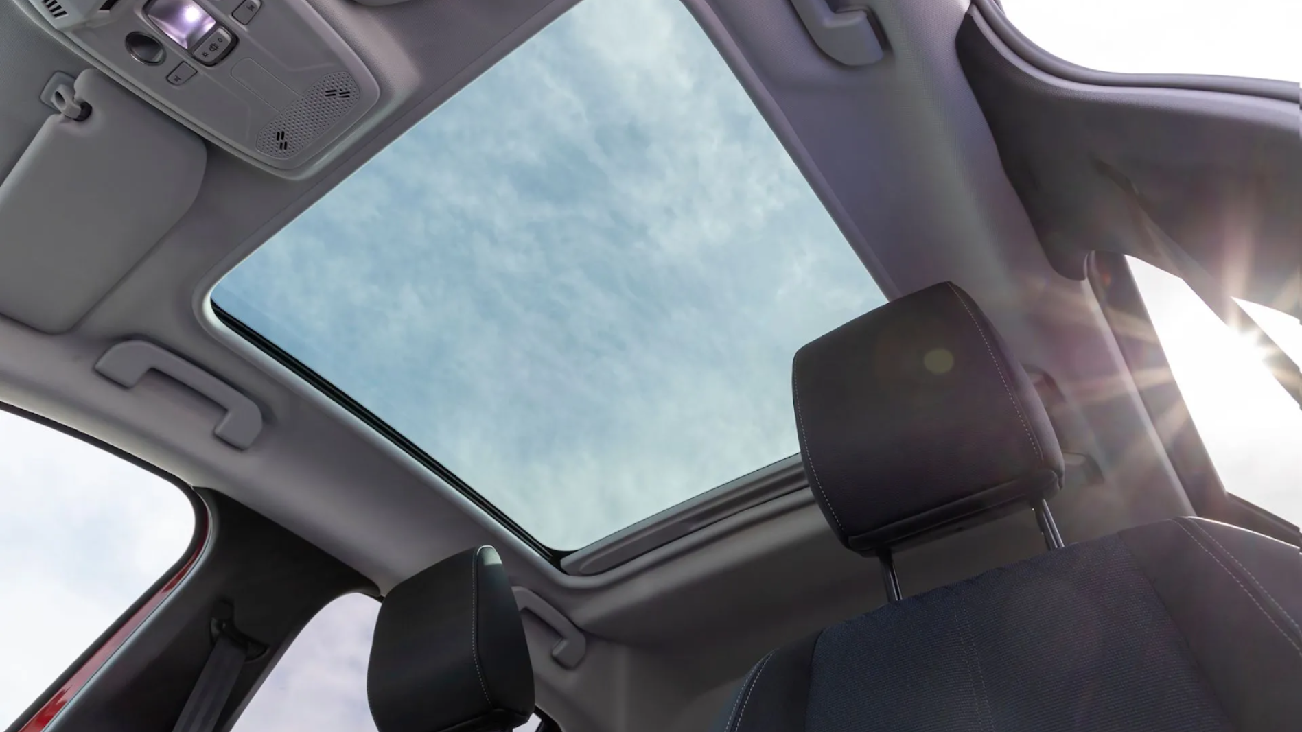 Interior car view with open sunroof; blue sky visible. Black headrests, white roof, and gray interior.