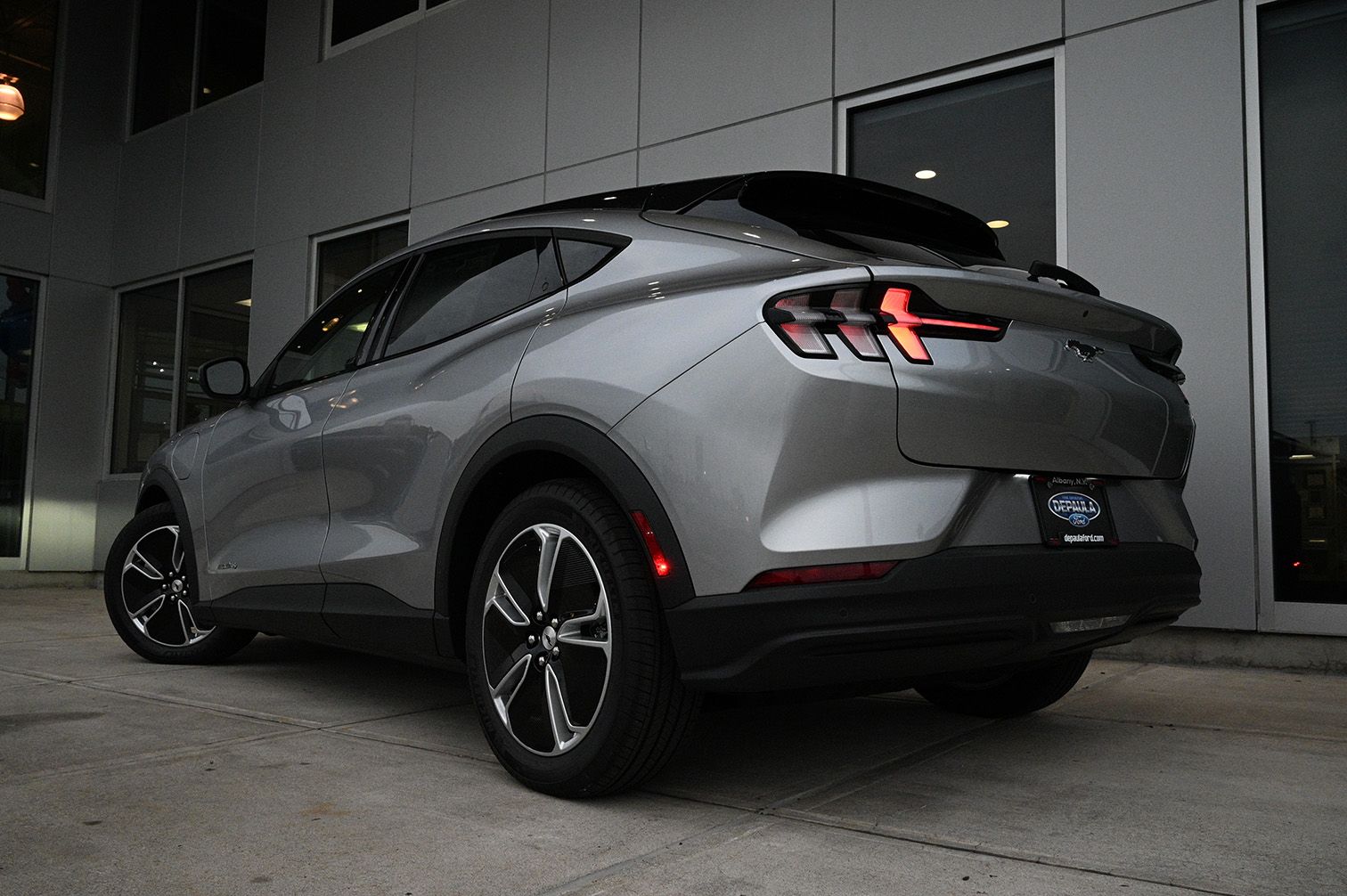 Silver Ford Mustang Mach-E electric SUV parked near a building with dark windows.