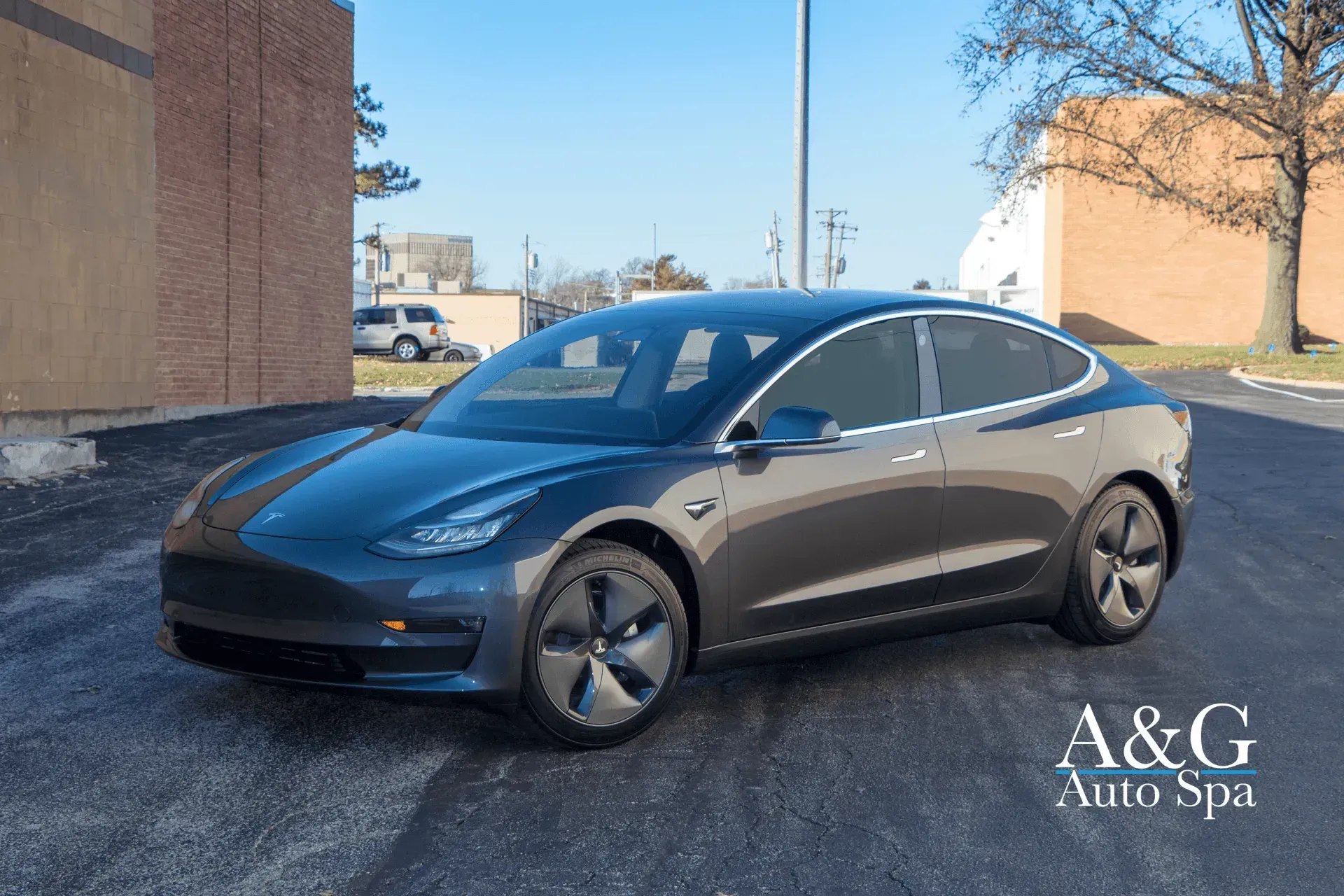 A tesla model 3 is parked in a parking lot in front of a building.