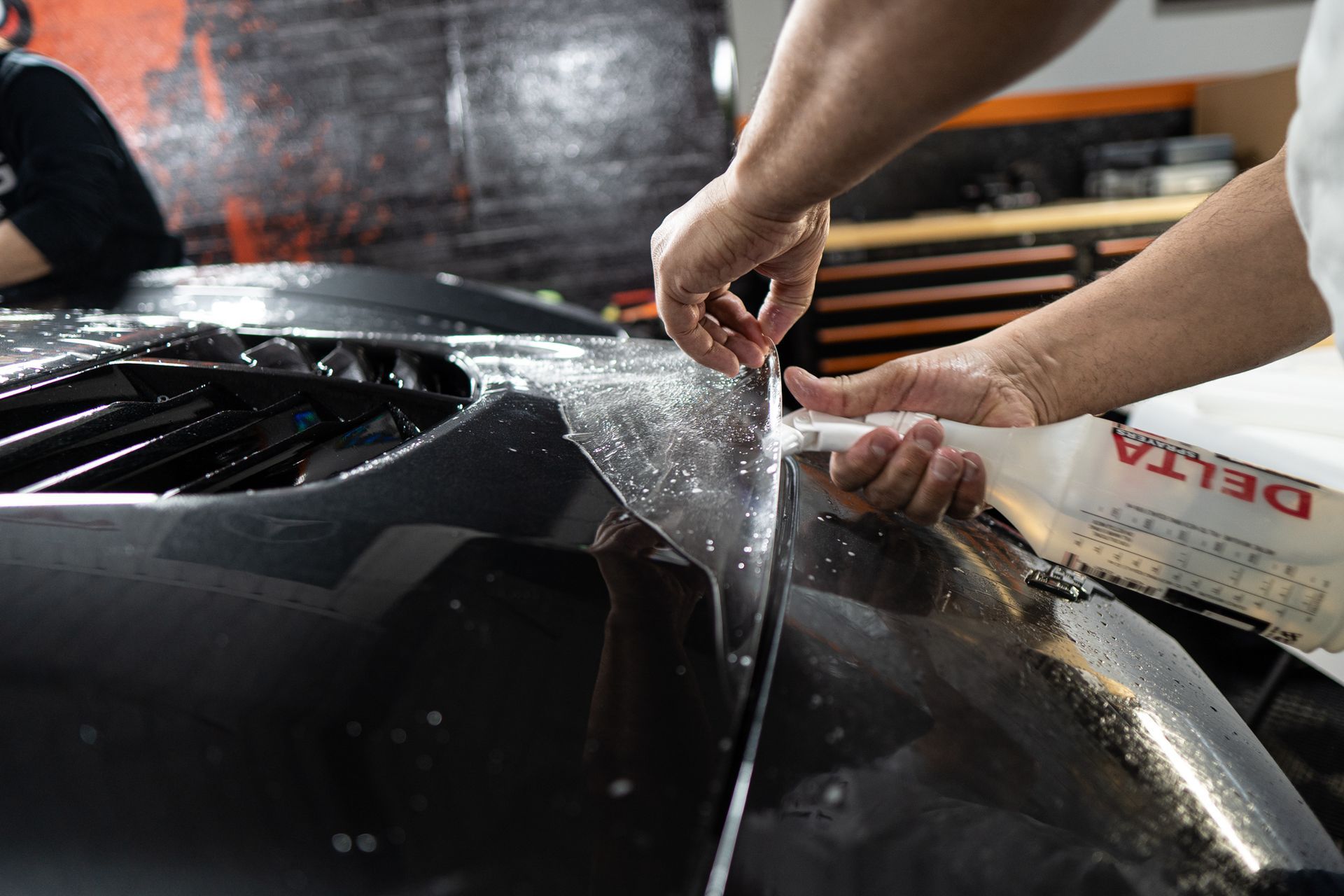 A man is applying a protective film to the hood of a car.