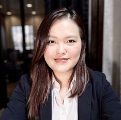 A woman with long black hair is wearing a black jacket and smiling.